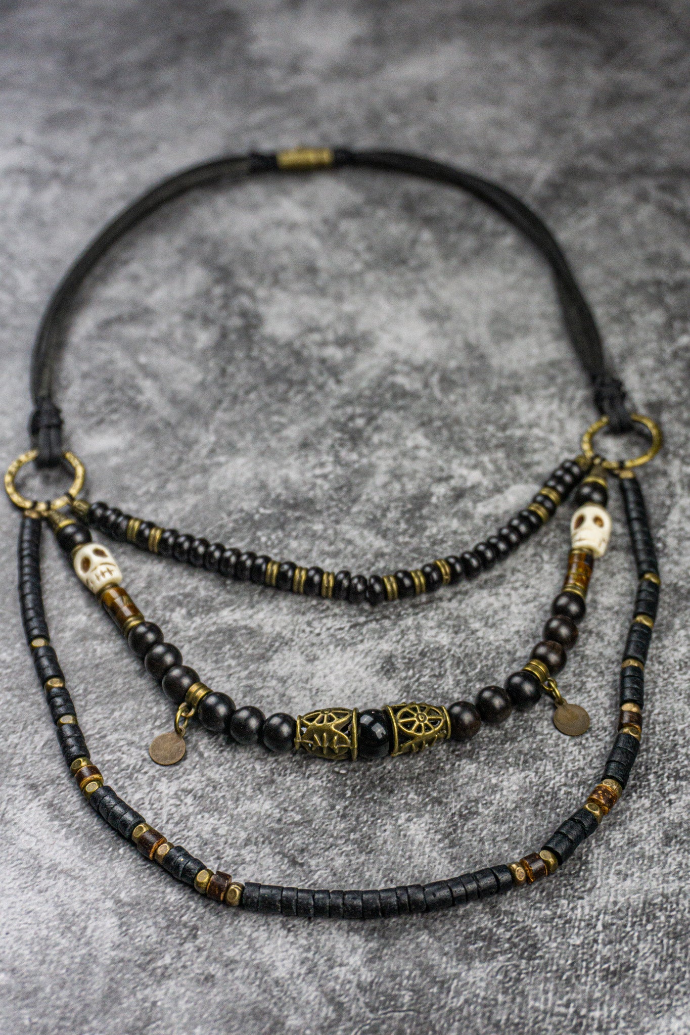 Layered beaded necklace with black and gold beads on a textured gray surface