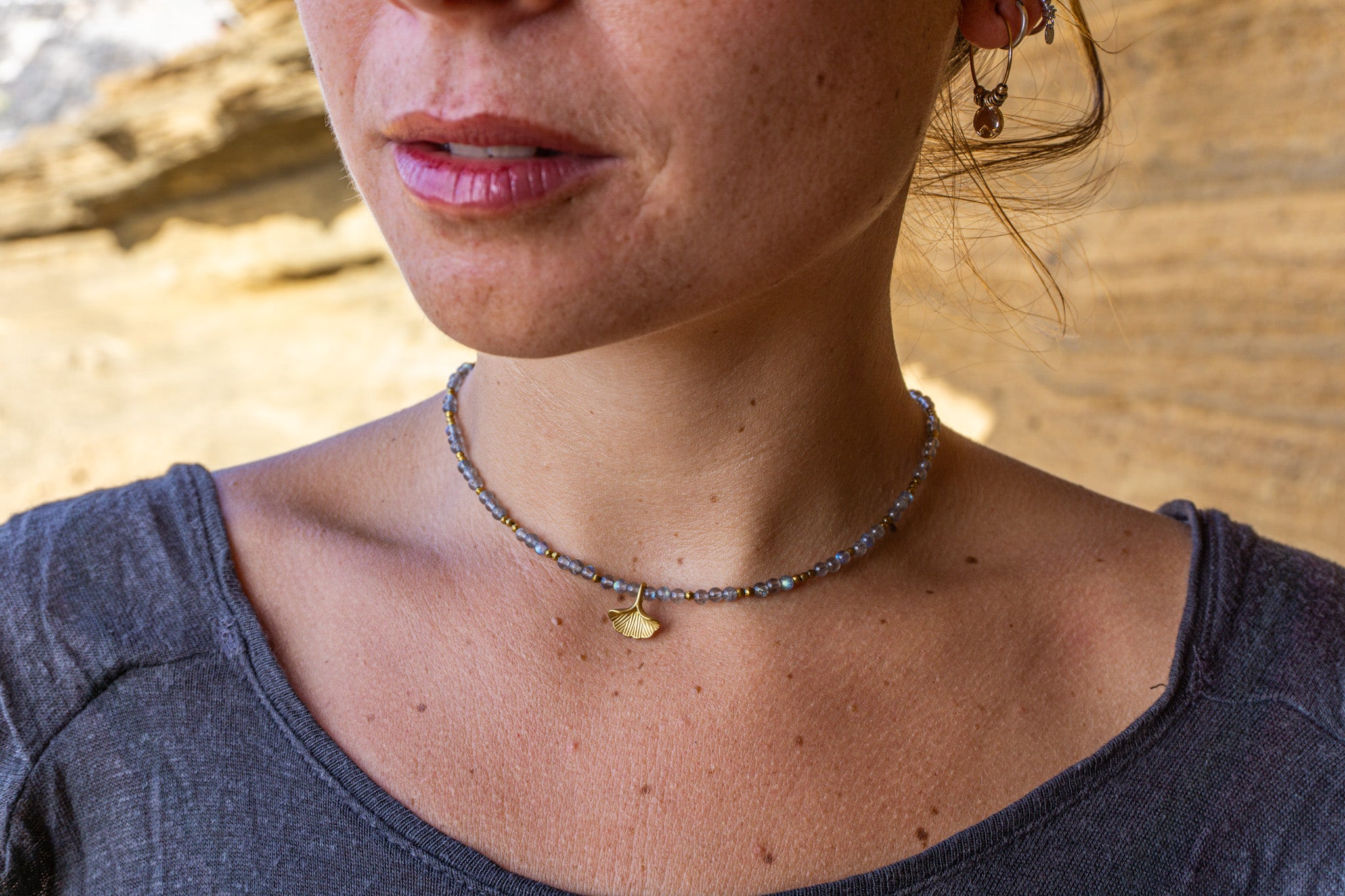 Close-up of a person wearing a choker necklace with a gold Ginkgo leaf charm against a blurred natural background- wander jewellery