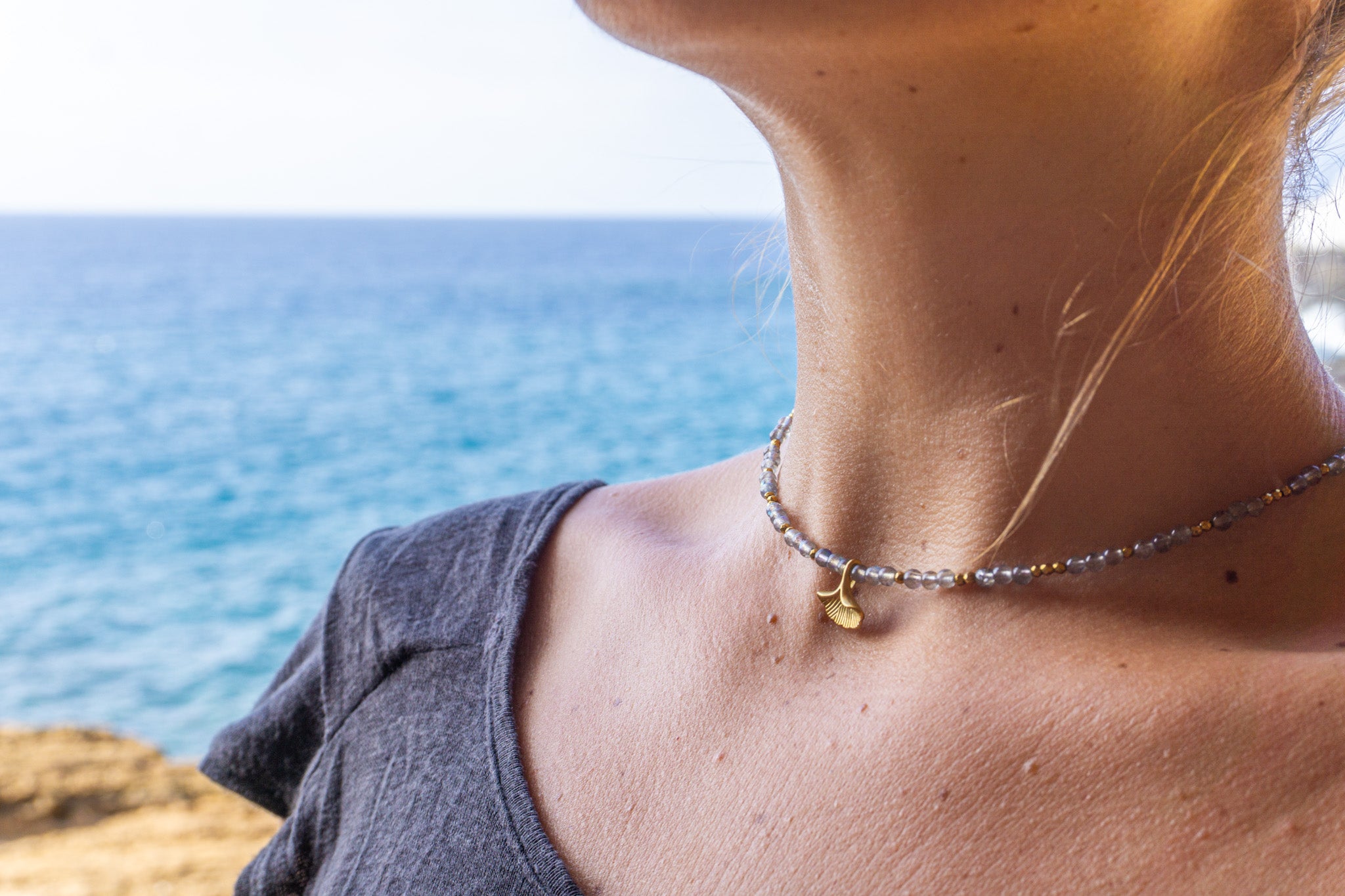 women wearing a labradorite choker pendant necklace with a blurred ocean background - Wander Jewellery