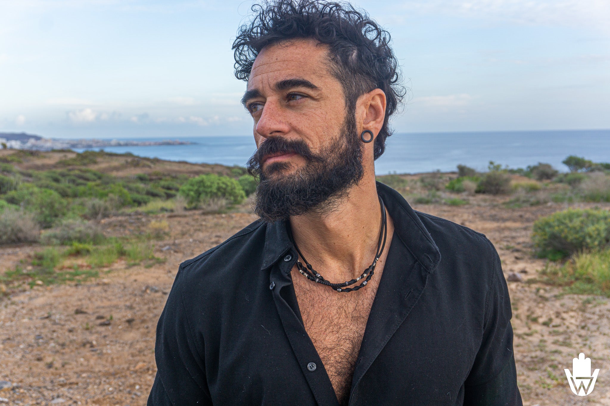 man in a scenografic landscape wearing black shirt ad a layered choker