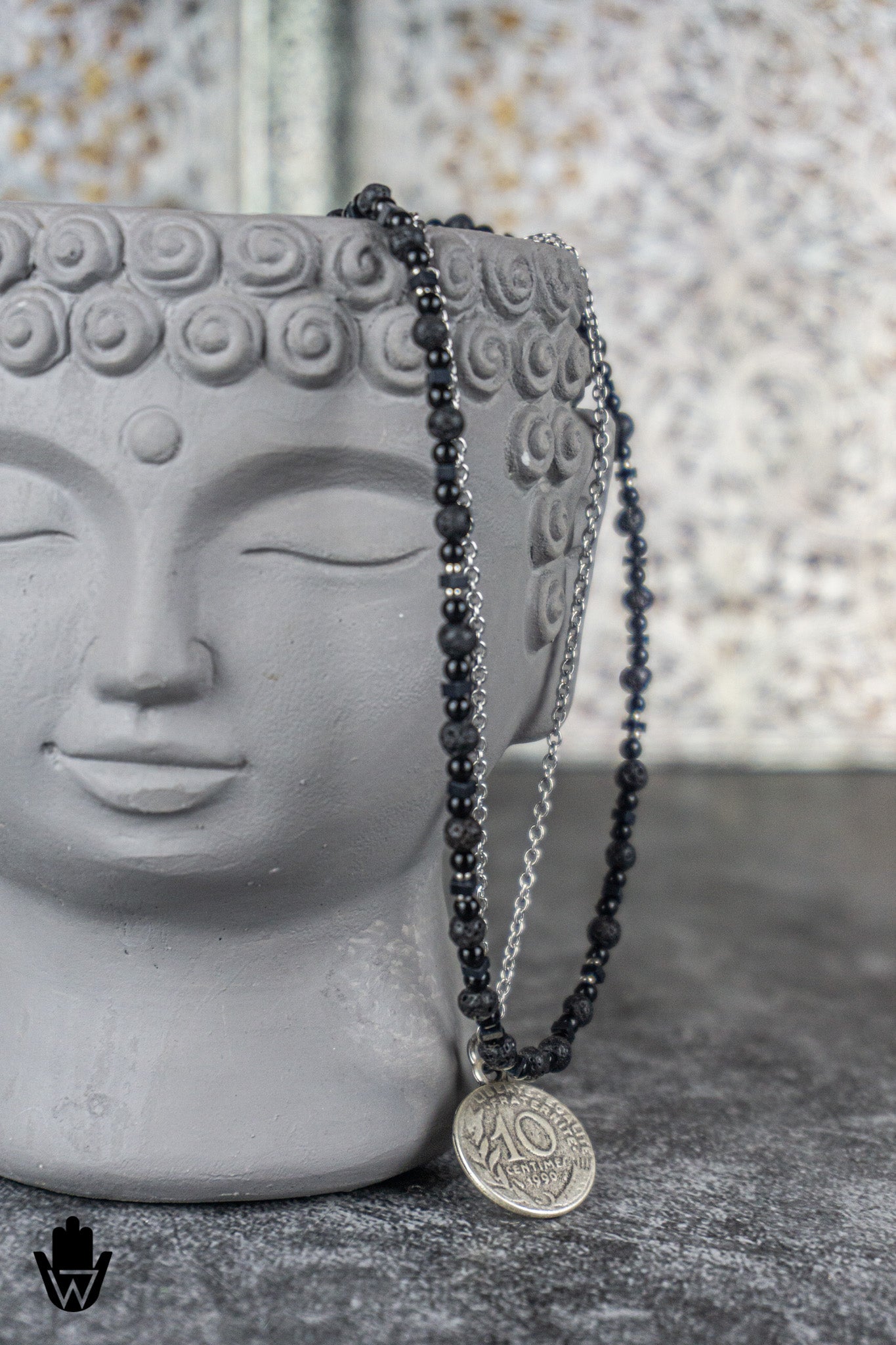A beaded necklace with black faceted beads, a silver chain, and a round silver coin pendant featuring the number 40, draped over a gray Buddha head statue.