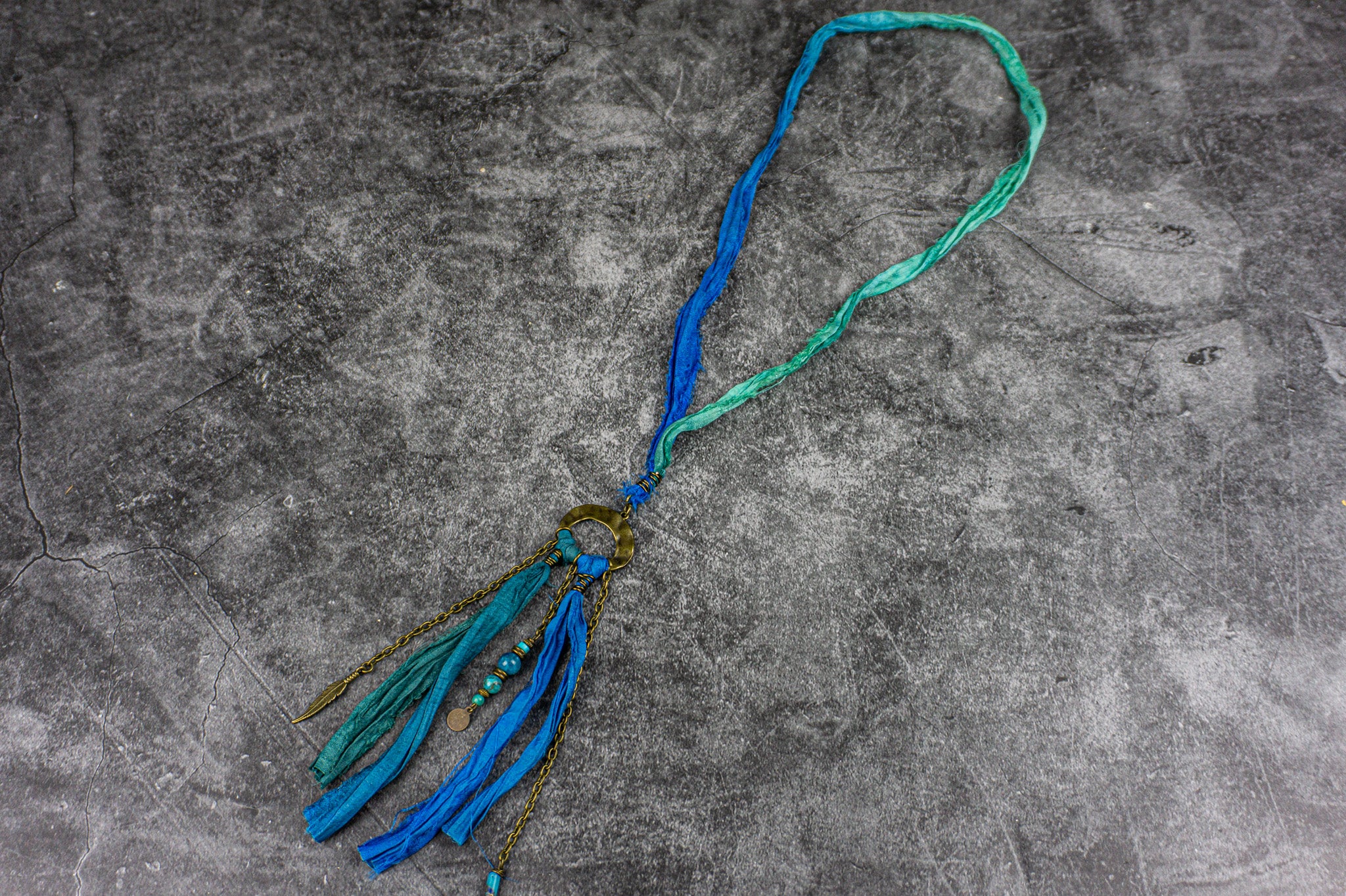 Long blue fabric necklace with brass hammered ring, silk fringes, and gemstone and chain charms – Wander Jewellery