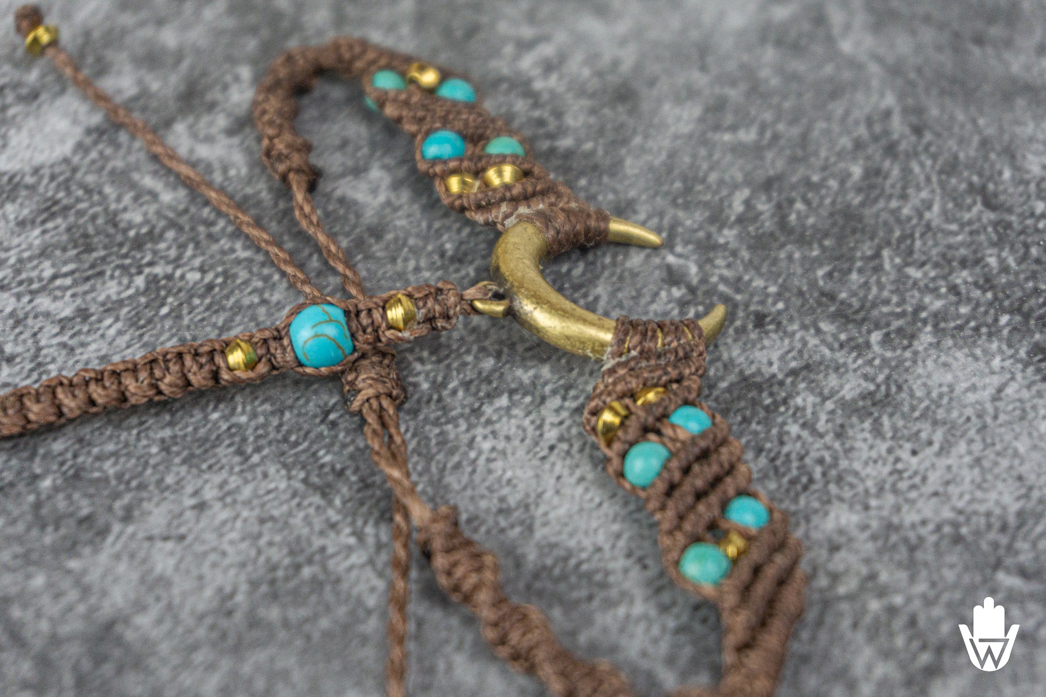 Brown macrame necklace with turquoise beads and gold accents on a gray surface