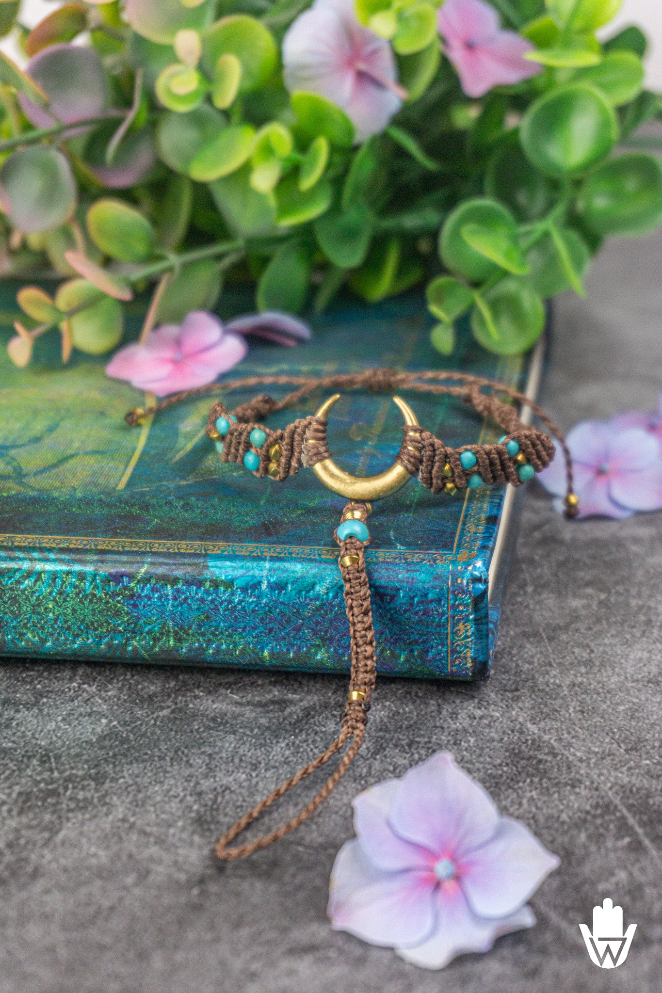 Bracelet with crescent moon design on a textured surface with flowers and a book