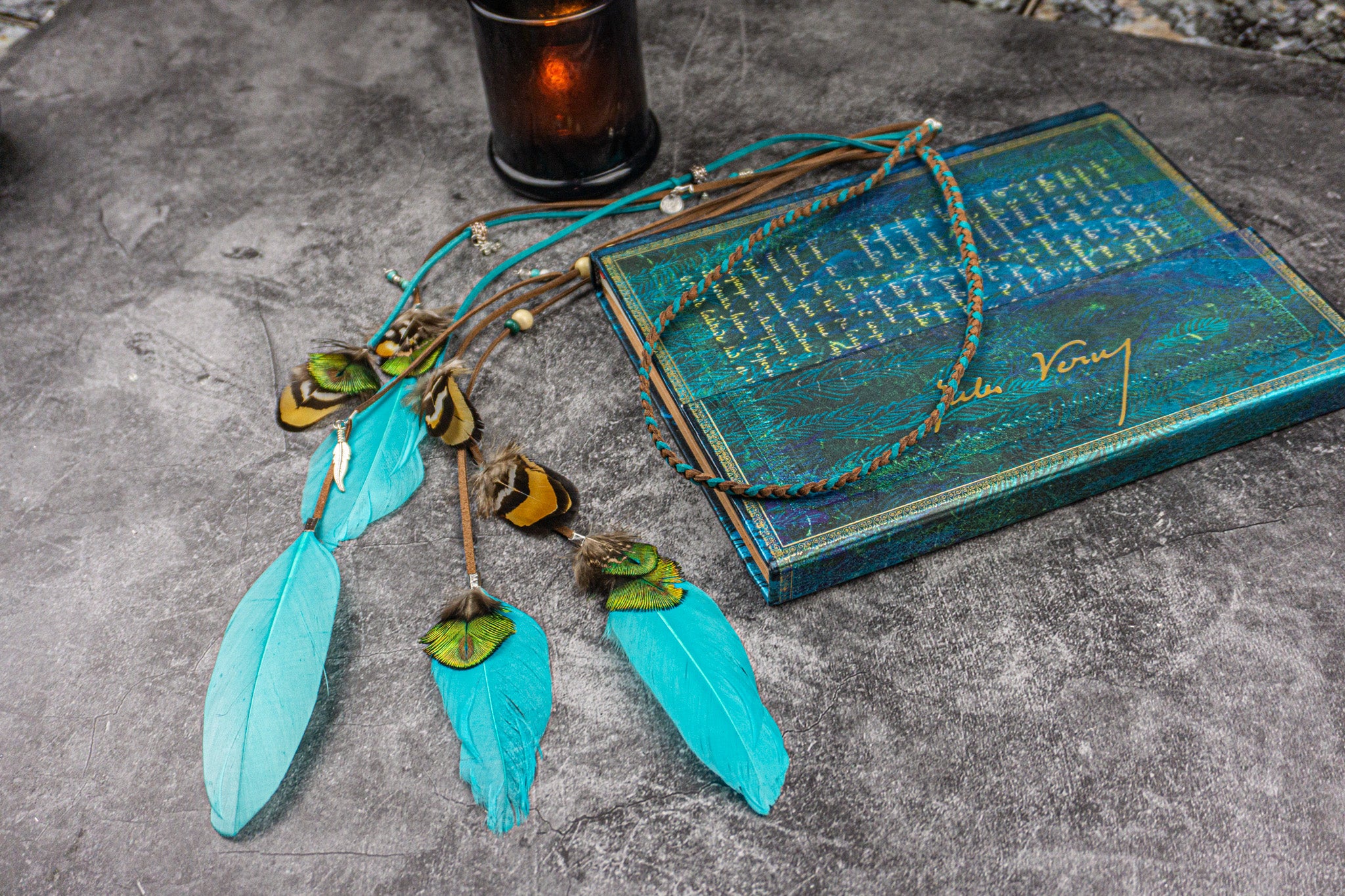 Turquoise feathered headband on a textured surface with a blue book and candle in the background.