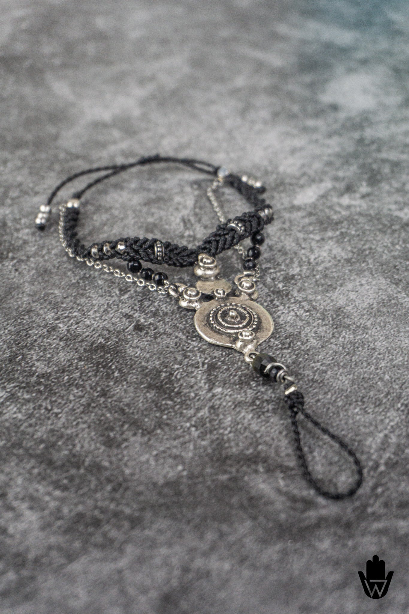 black bracelet with macrame braided design and decorative silver elements on a textured gray surface