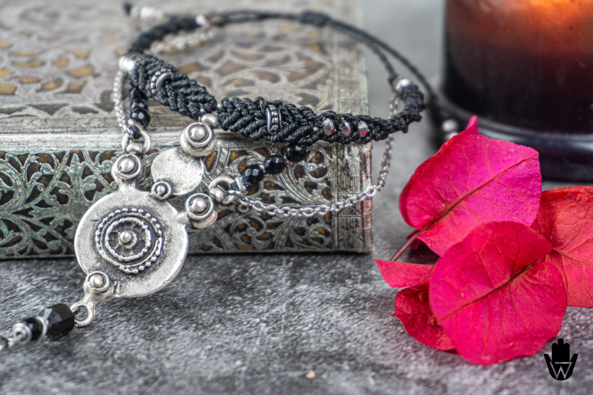 Silver bracelet with black braided cord and red flower on a textured surface