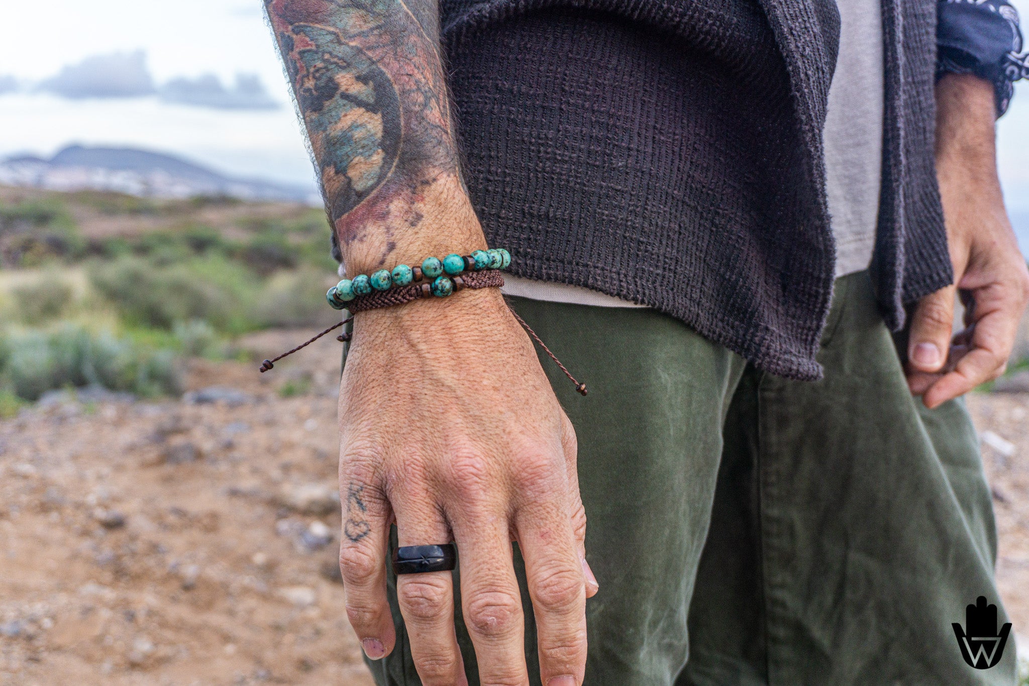 Person wearing a black ring and green beaded bracelet set with a desert landscape in the background