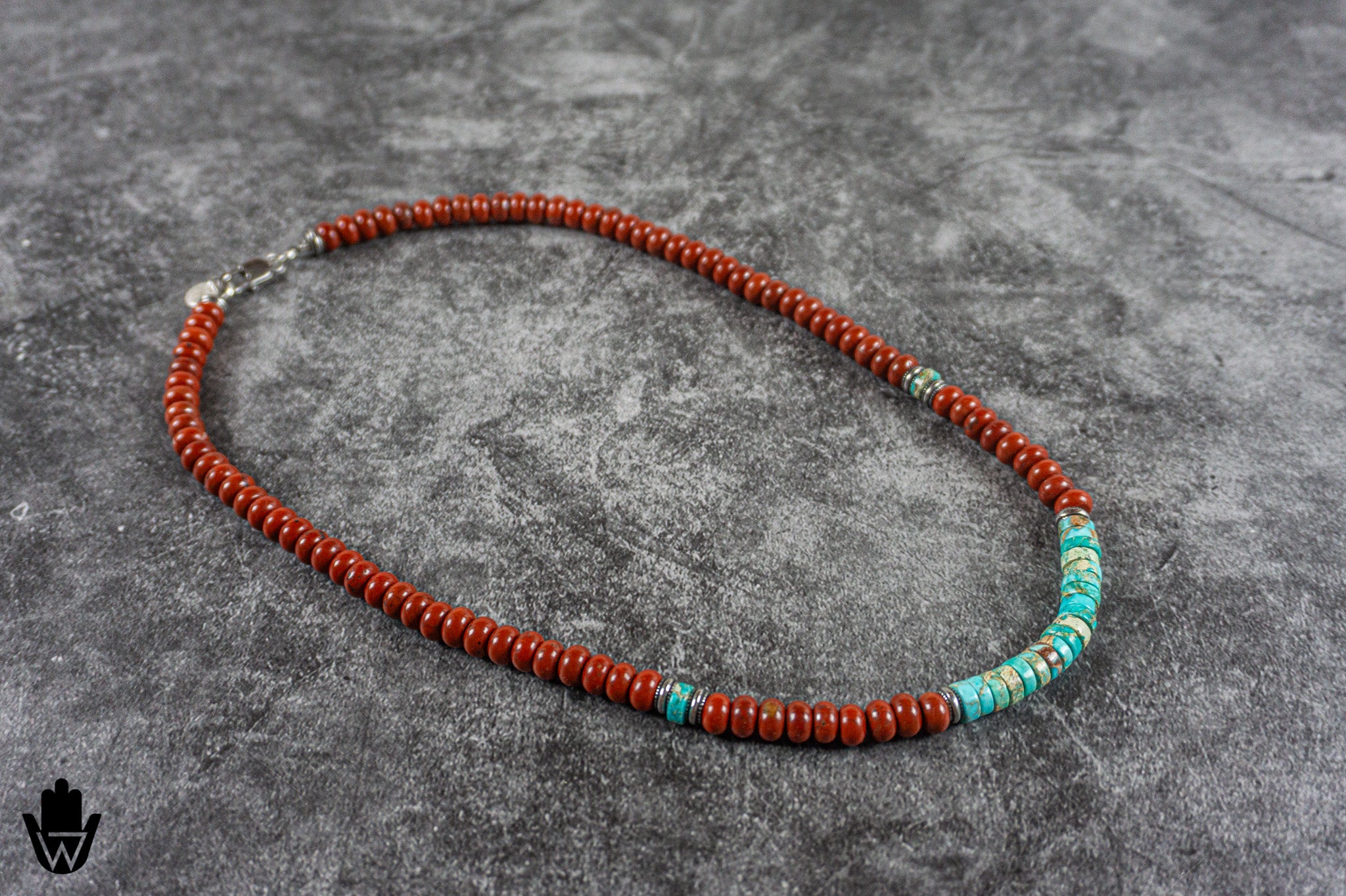 A beaded necklace featuring reddish-orange beads with turquoise and white accents, displayed on a textured gray background.