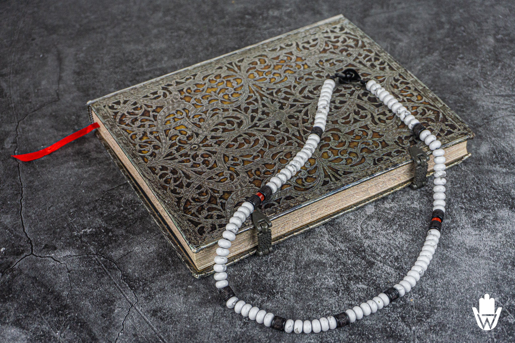 white black and red necklace sitting on a silver colored book