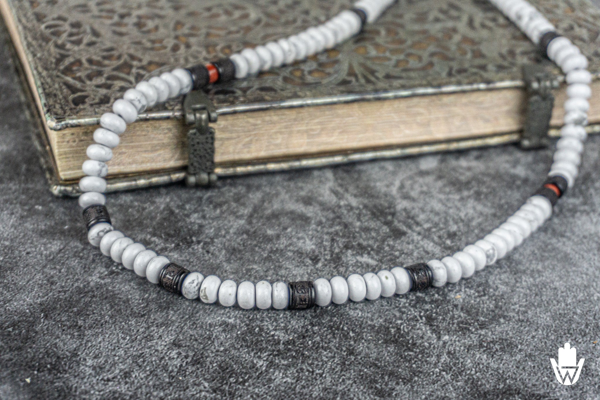 close up to a white beaded necklace with buddhist details