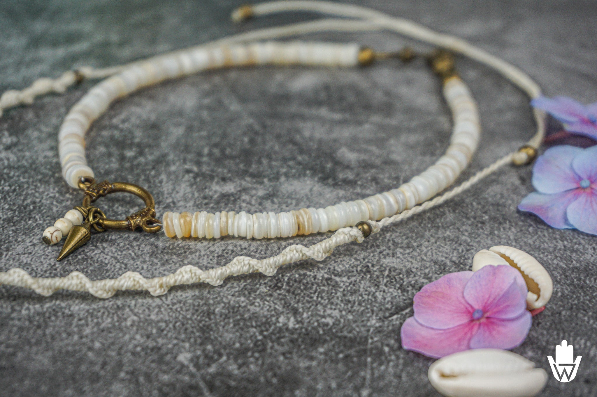 close up of a white necklace set on a grey surface with flowers