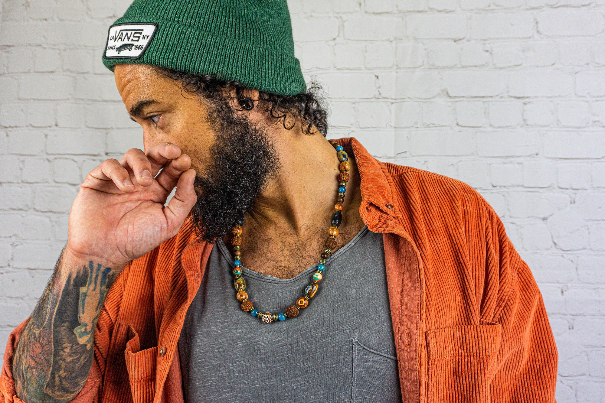 Man wearing a green beanie and orange jacket against a white brick wall