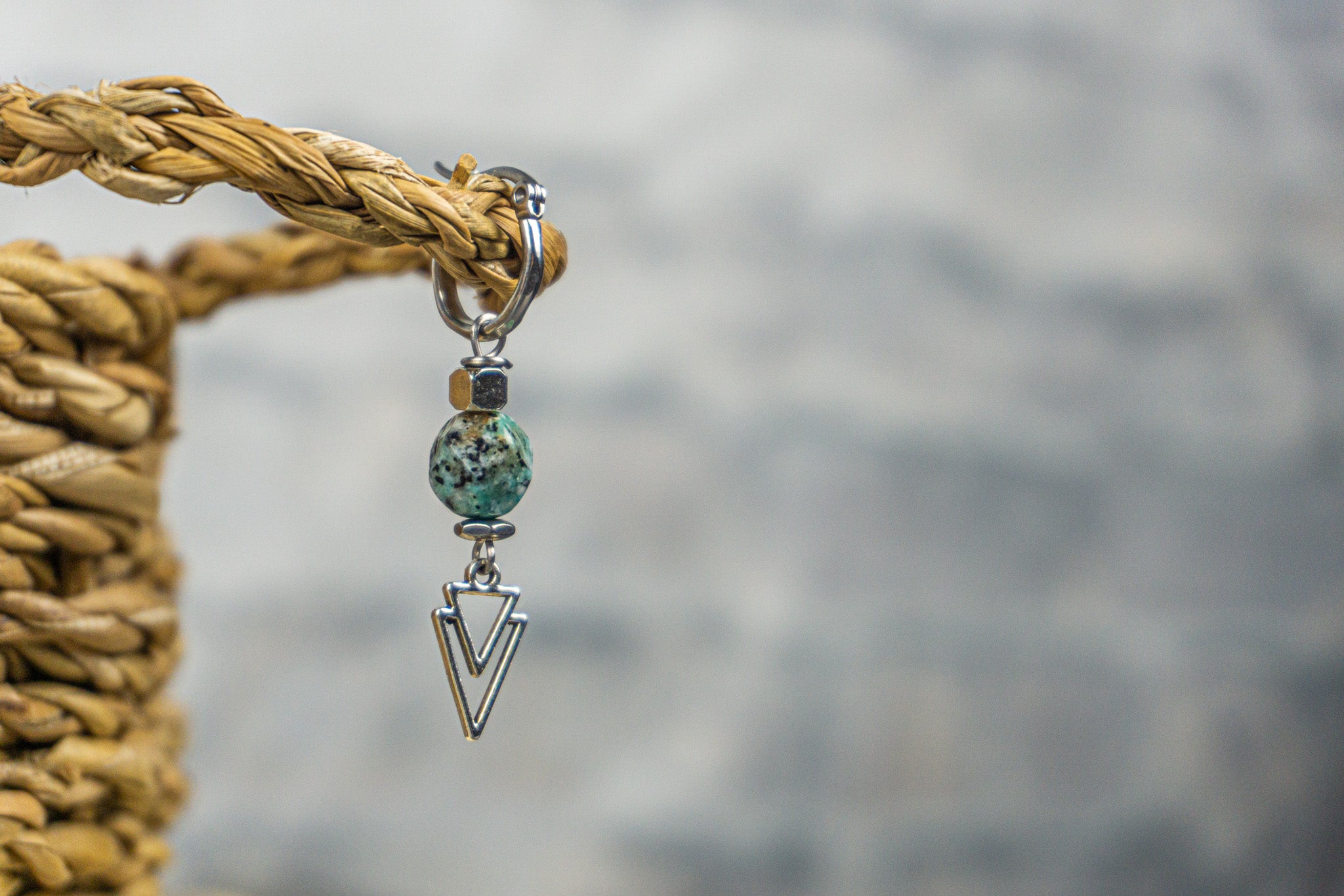 A silver colored earring with a green blue gemstone and geometric charm