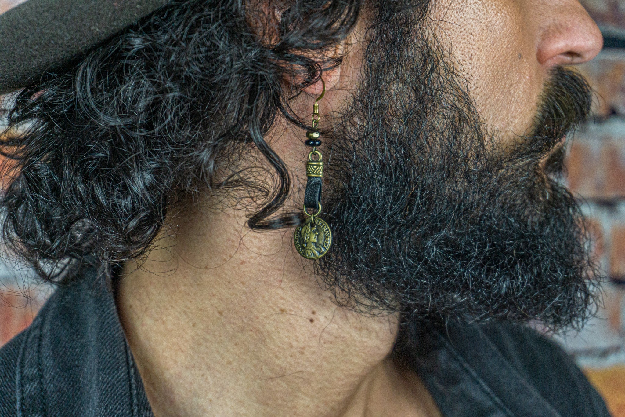men with long hair and beard, hat, black jacket and a leather earring with an ancient coin