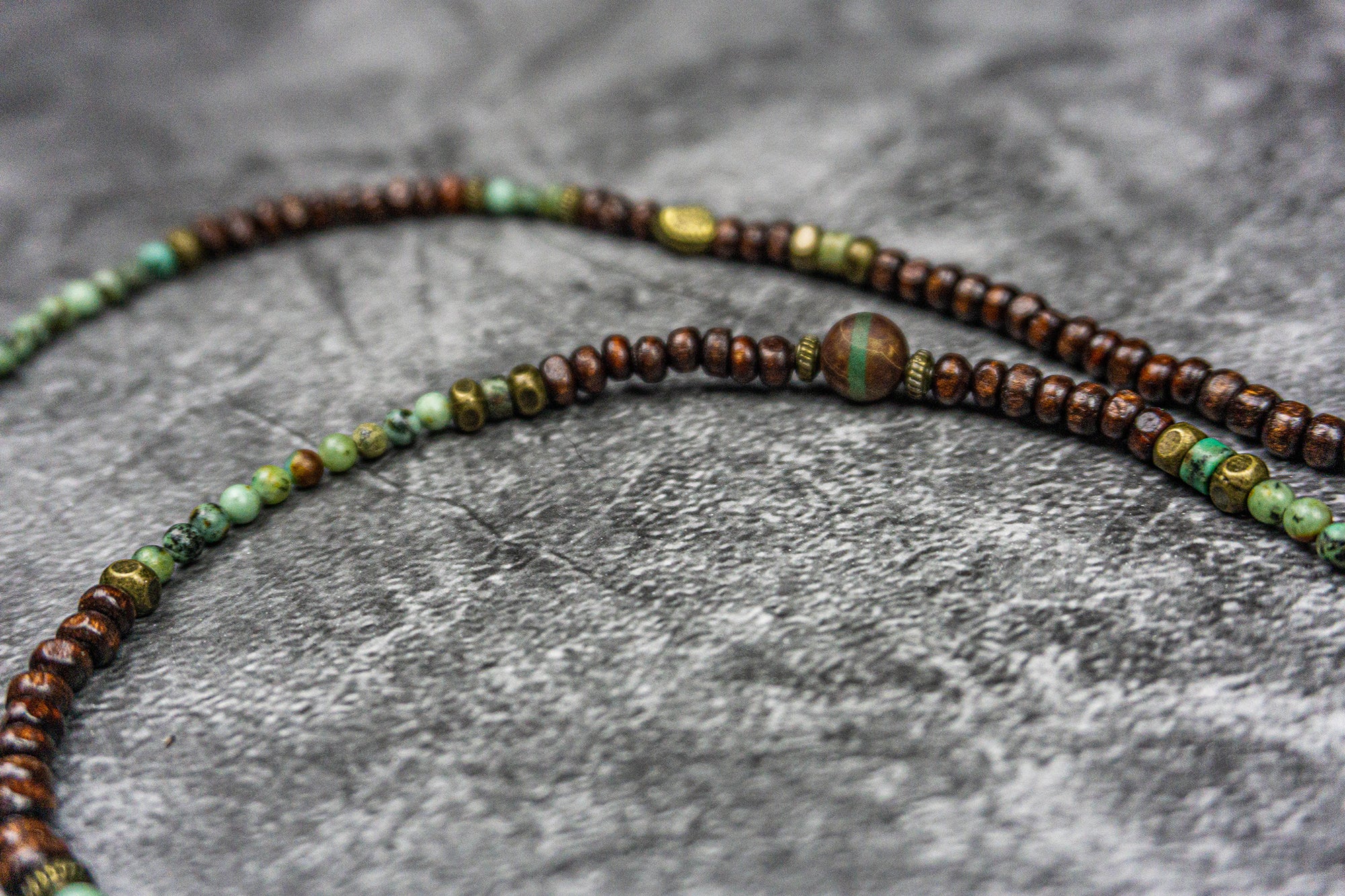close picture of a necklace made of wood and green gemstone bads, agate and bronze deatils- wander jewellery