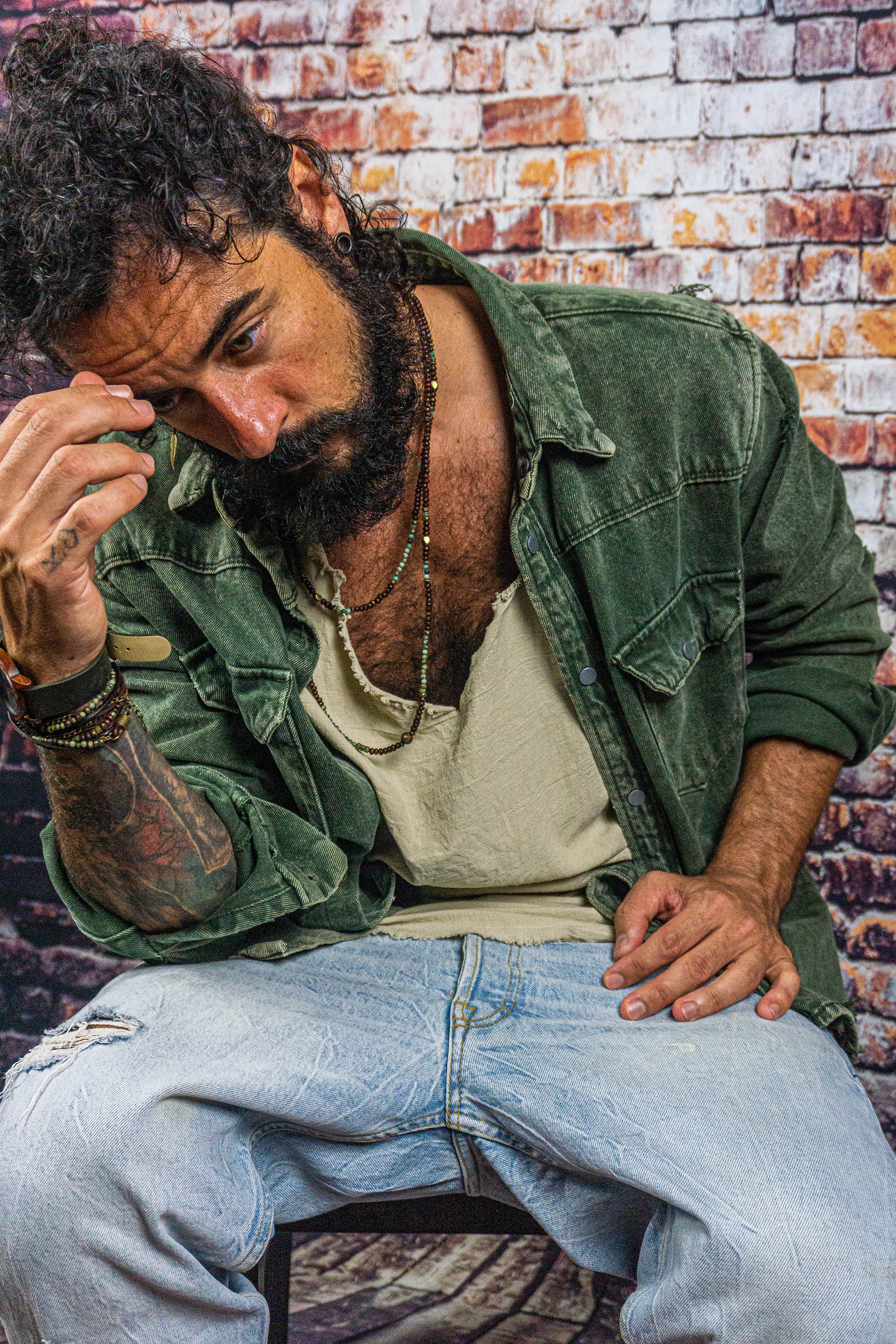 sitting mens waering a long layered necklace made of wood and green gemstone bads- wander jewellery