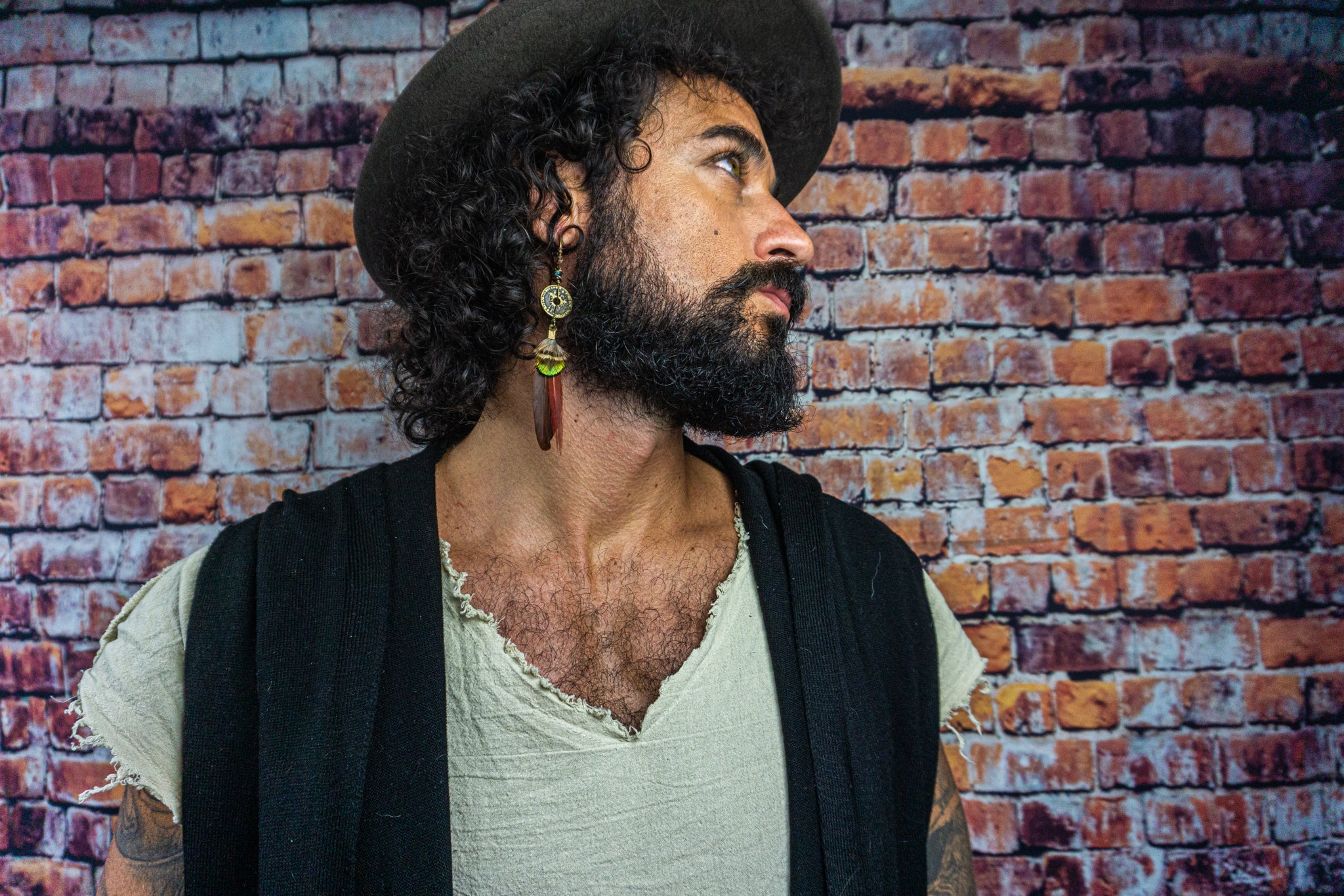 mens with a hat wearing red and green feather earring with a coin charm- Wander Jewellery