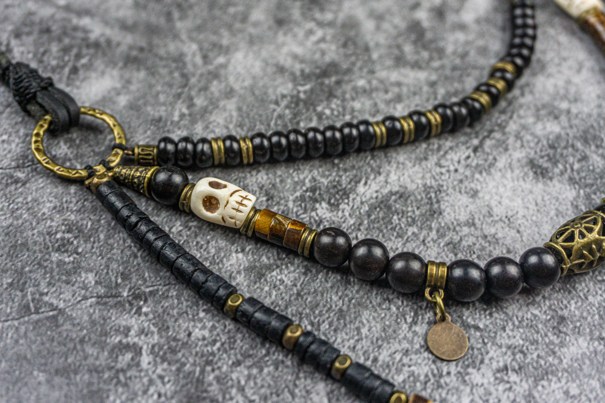 Black beaded necklace with gold accents and a skull charm on a gray surface