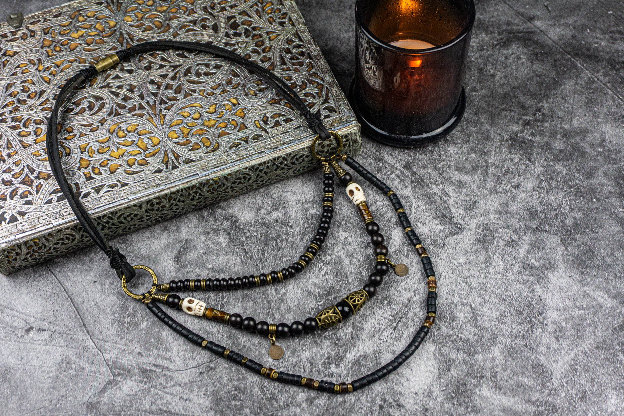 Black beaded necklace with gold accents on a textured surface with a candle in the background