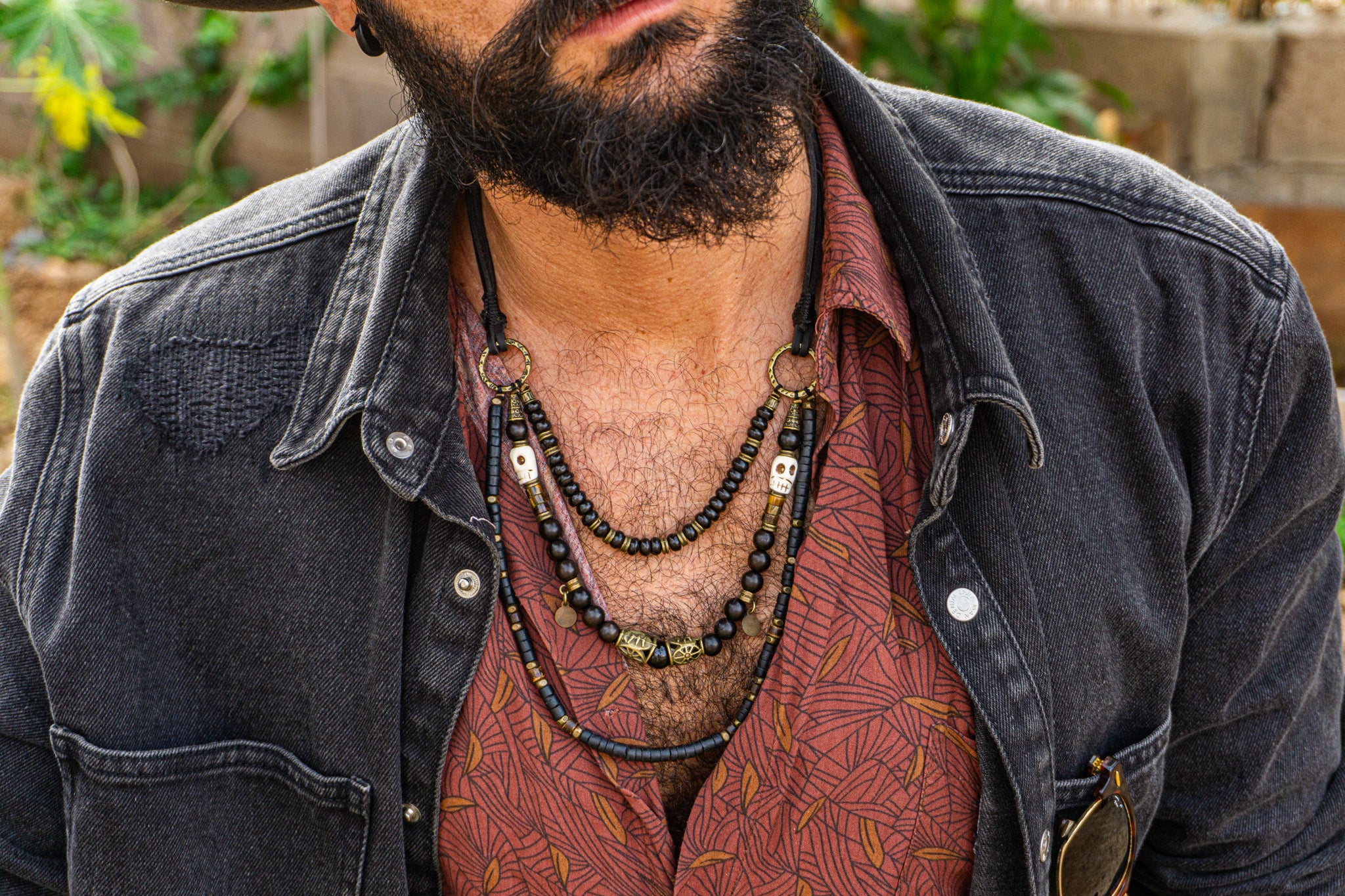 Man wearing a dark denim jacket and patterned shirt with a necklace set.
