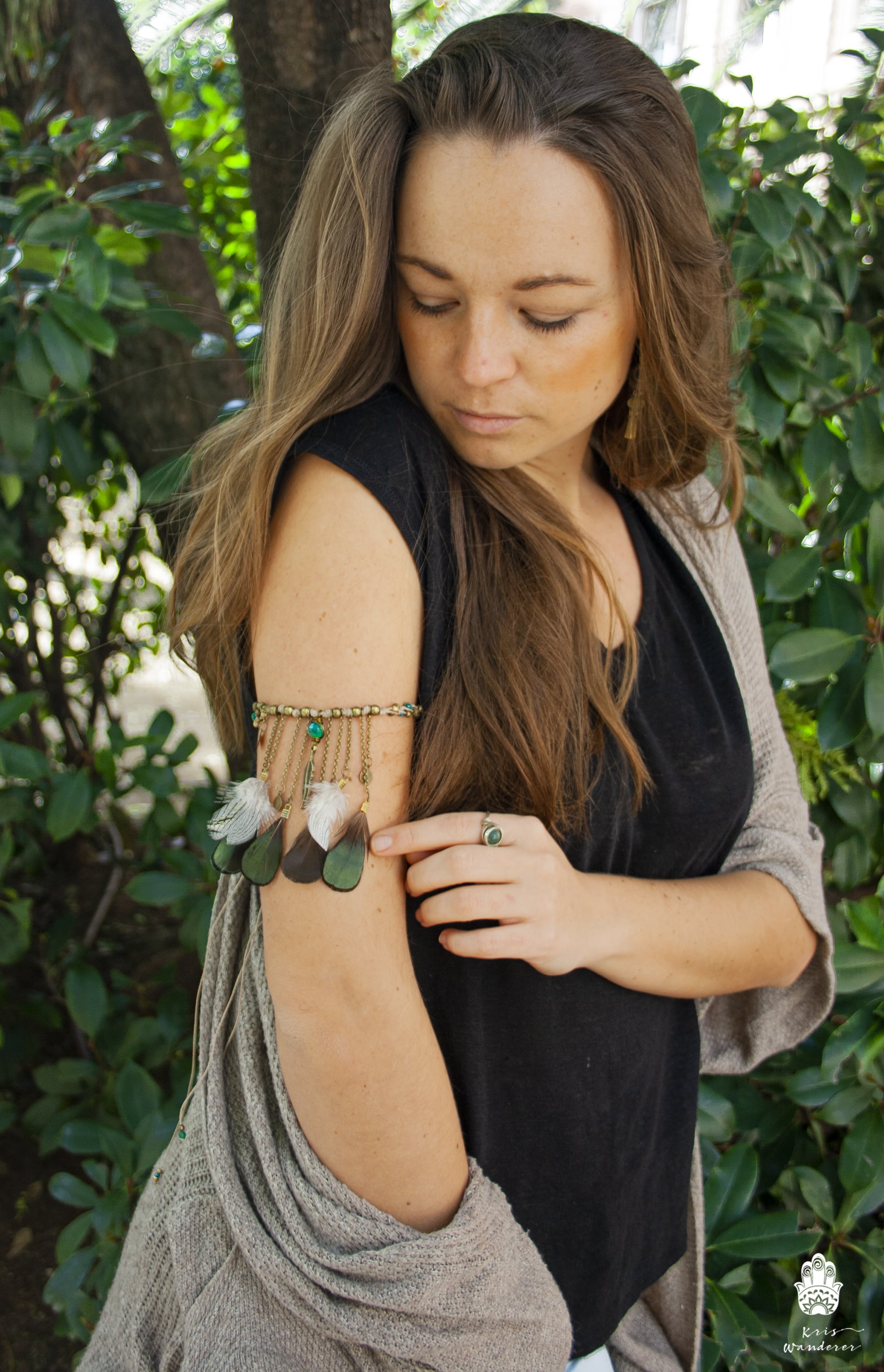 Woman wearing a black sleeveless top and gray cardigan with greenery in the background