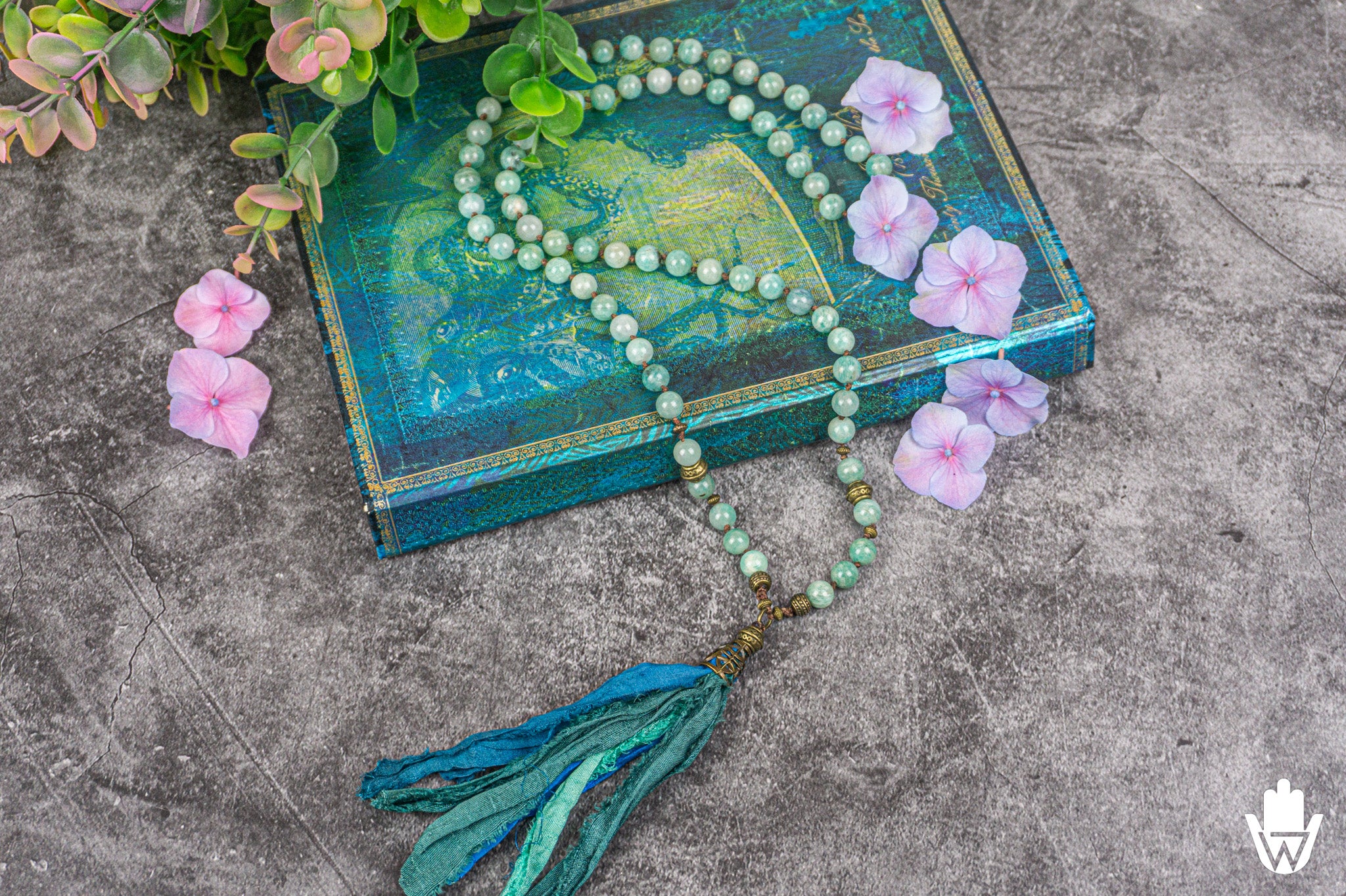 amazonite gemstone necklace sitting on a blue and golden book decorated with pink flowers