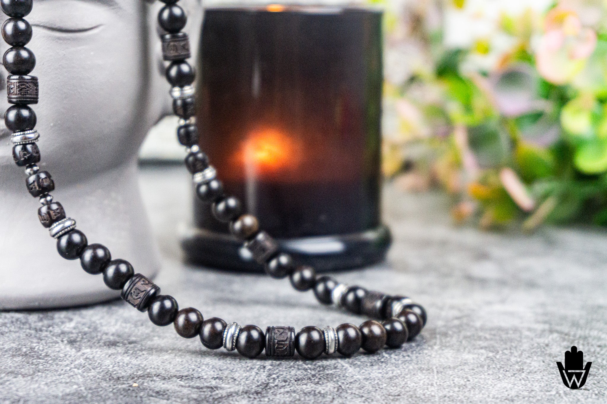 A beaded necklace with dark brown and black round beads, accented by silver-toned spacer beads, draped over a gray mannequin head and a dark amber candle in a real setting.