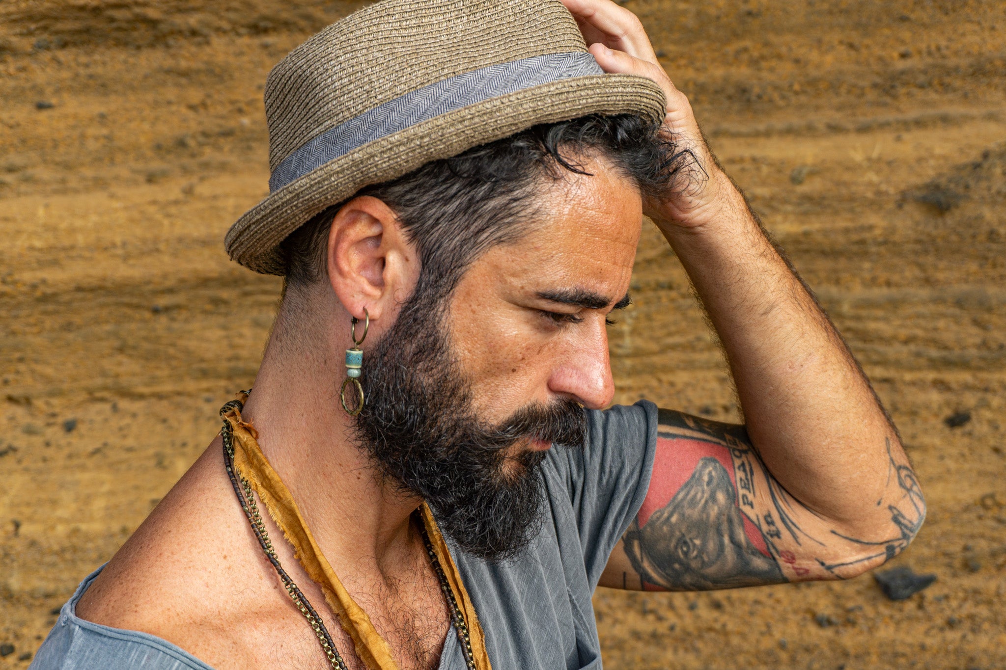 Man with a beard and tattoos wearing a straw hatwit a dangle hoop beaded earring- wander jewellery