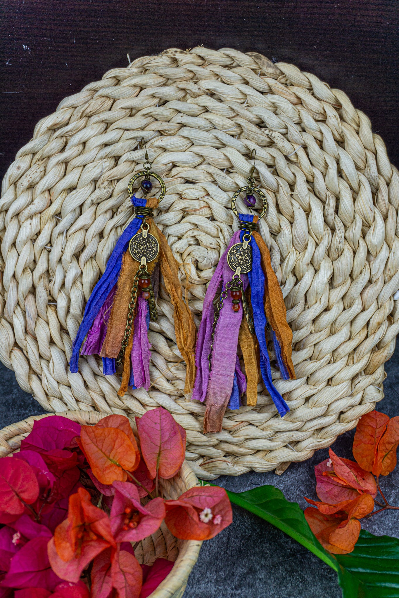 Colorful boho tassel earrings on a woven mat with flowers in the foreground