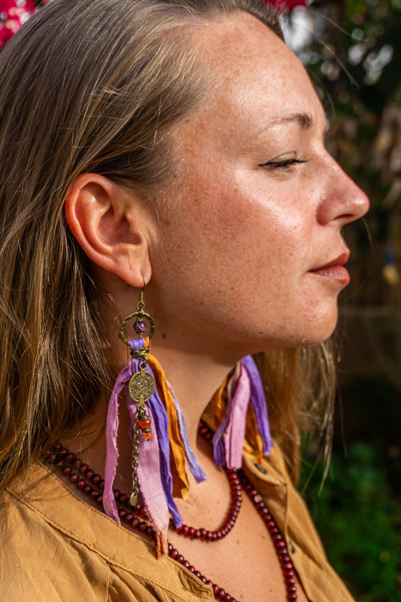 Close-up of a woman wearing colorful earrings with brass charms and dangle chain-wander jewellery