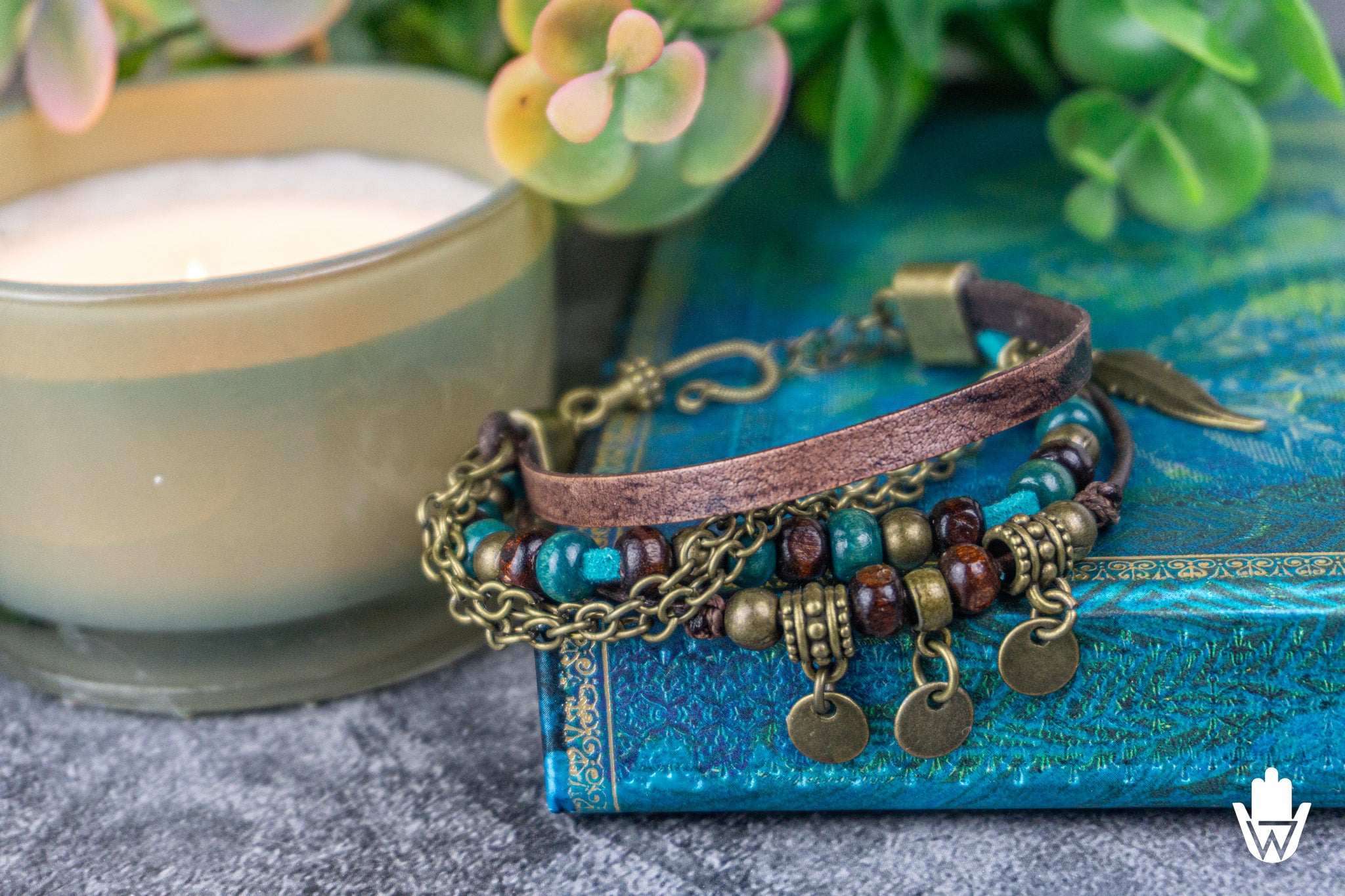 Layered bracelet with beads and charms on a blue surface next to a candle