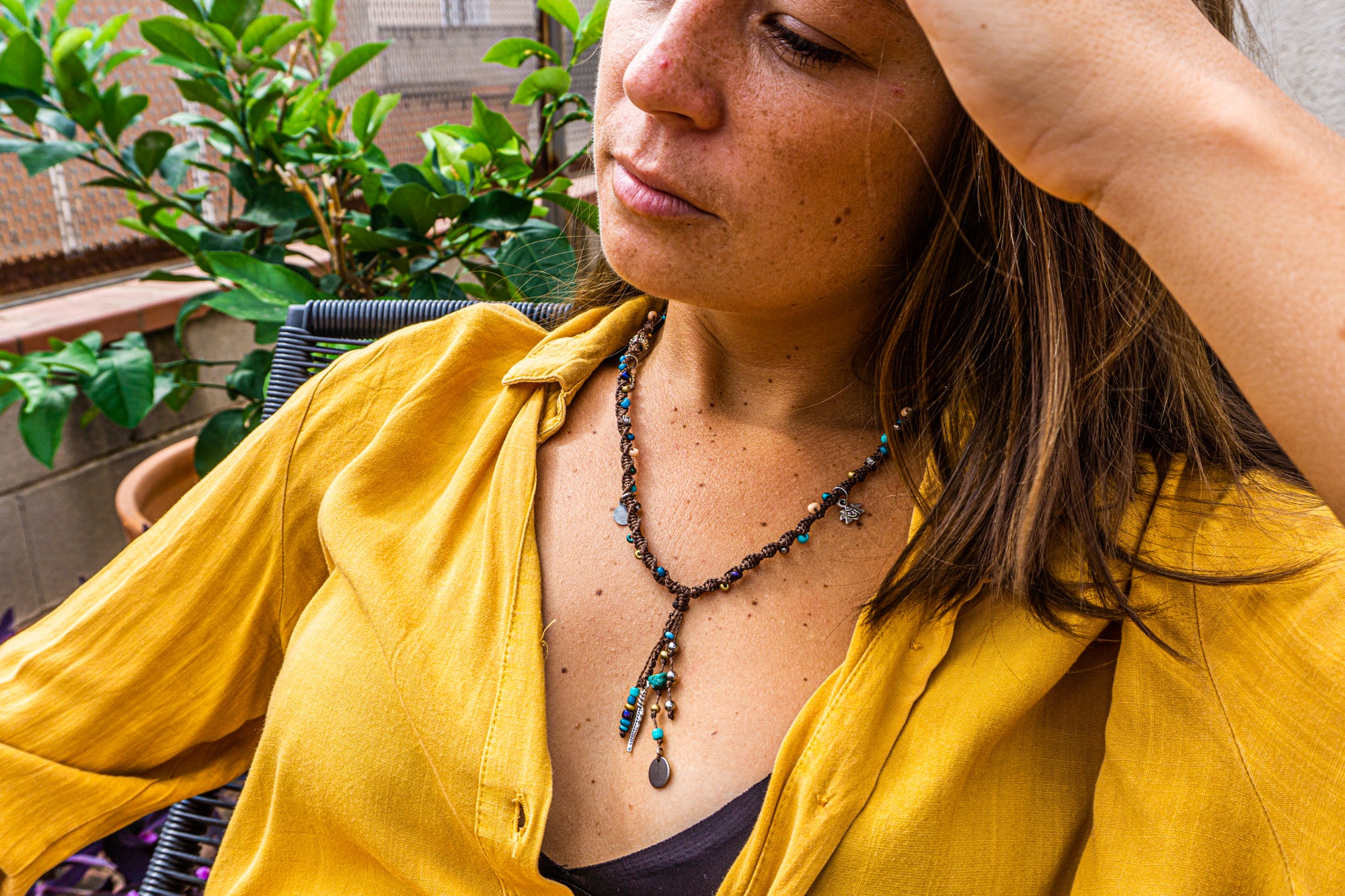 Woman wearing a yellow shirt and a necklace with a plant in the background