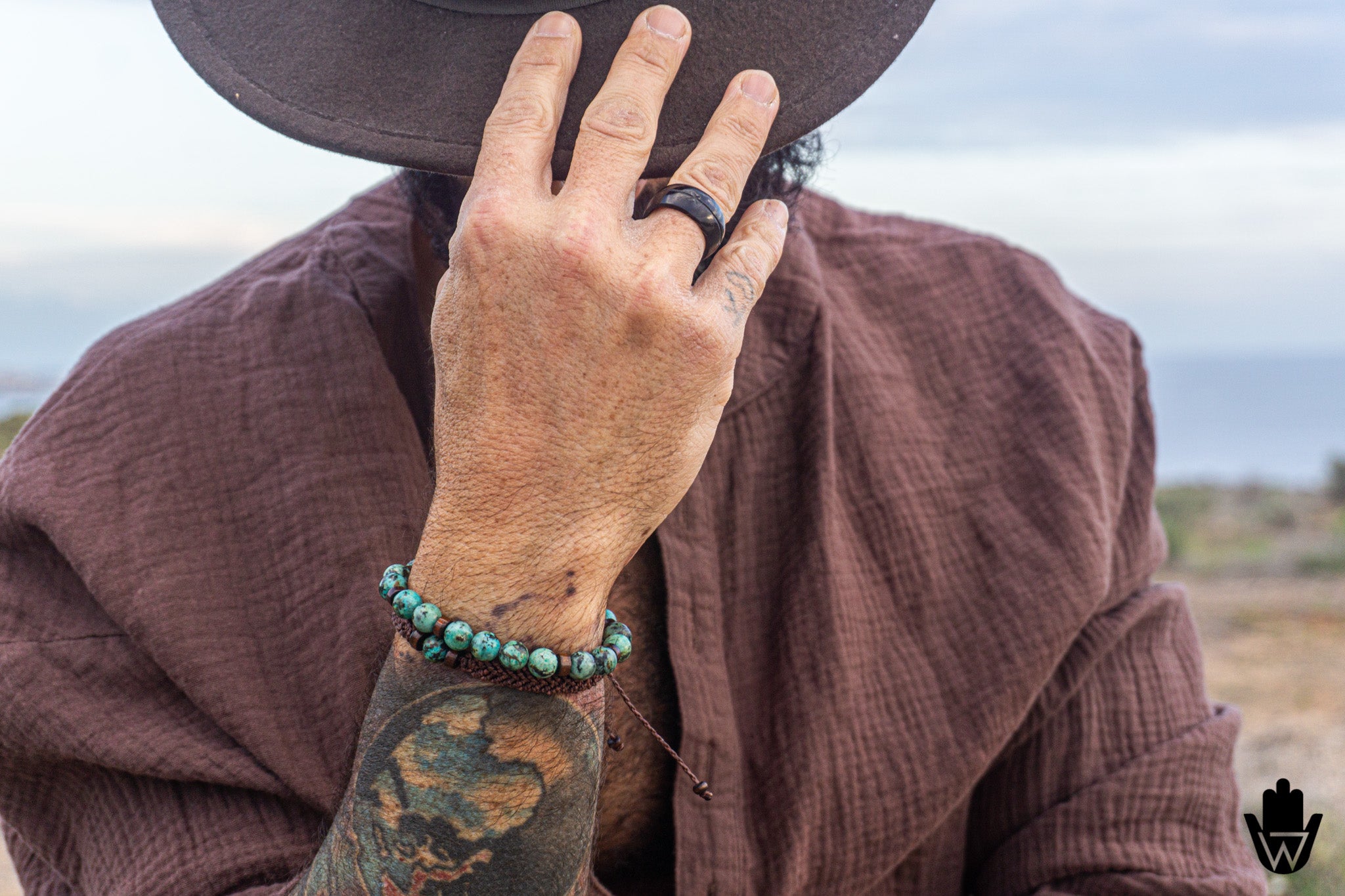 Person wearing a wide-brimmed hat, brown shirt, and turquoise bracelet with a tattooed arm.
