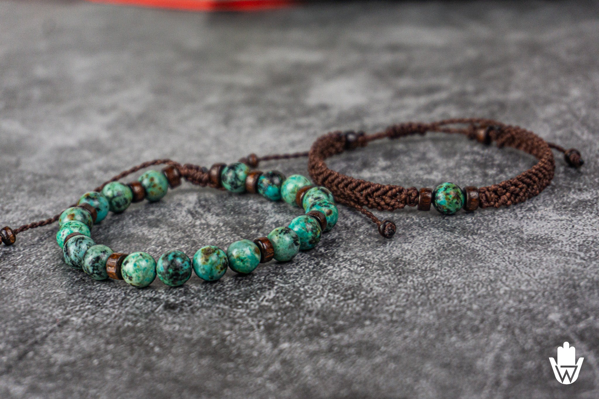Two matching bracelets with green beads and brown braided straps on a gray surface