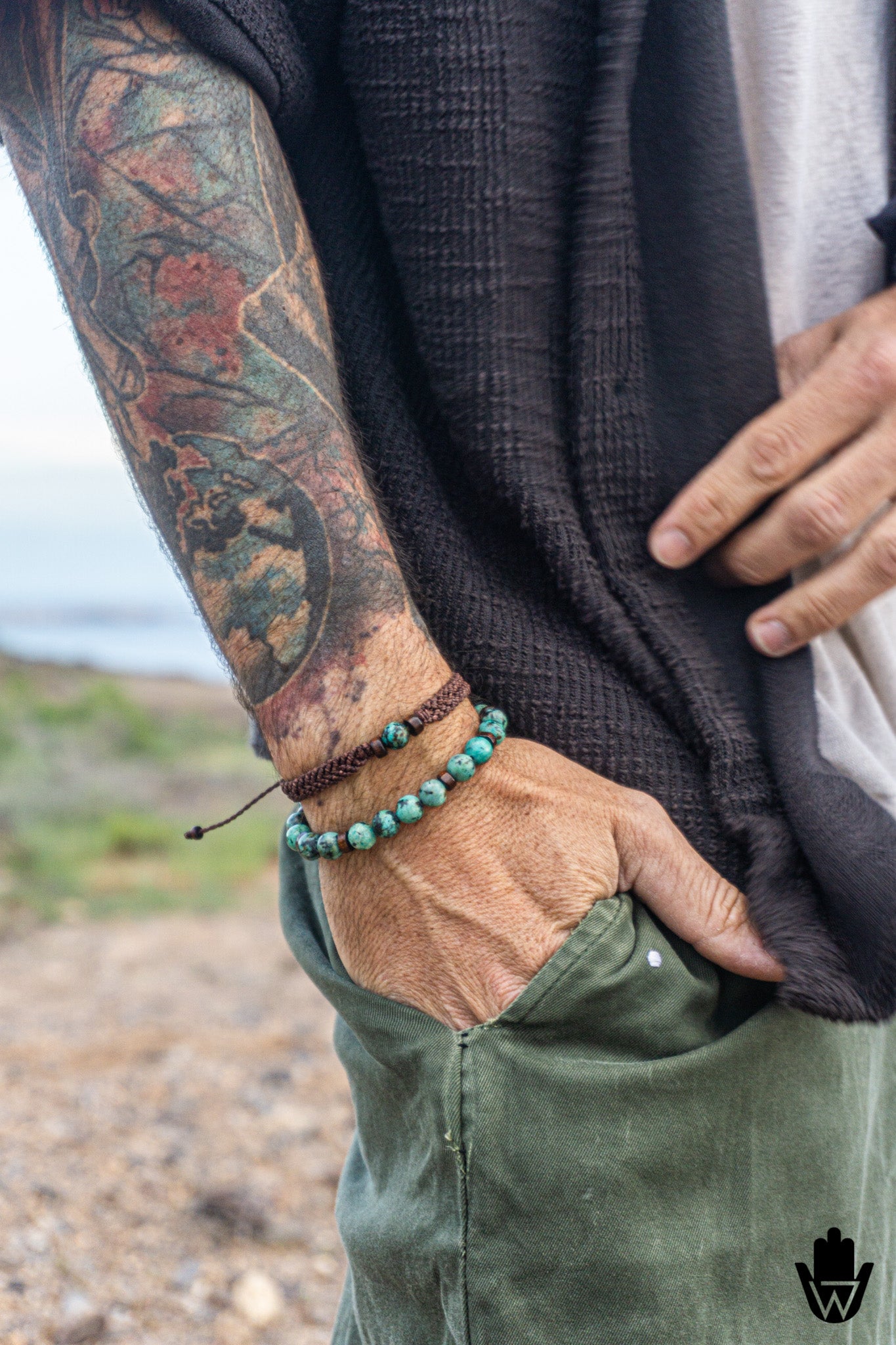 Person wearing a green beaded bracelet with a tattooed arm, standing outdoors.