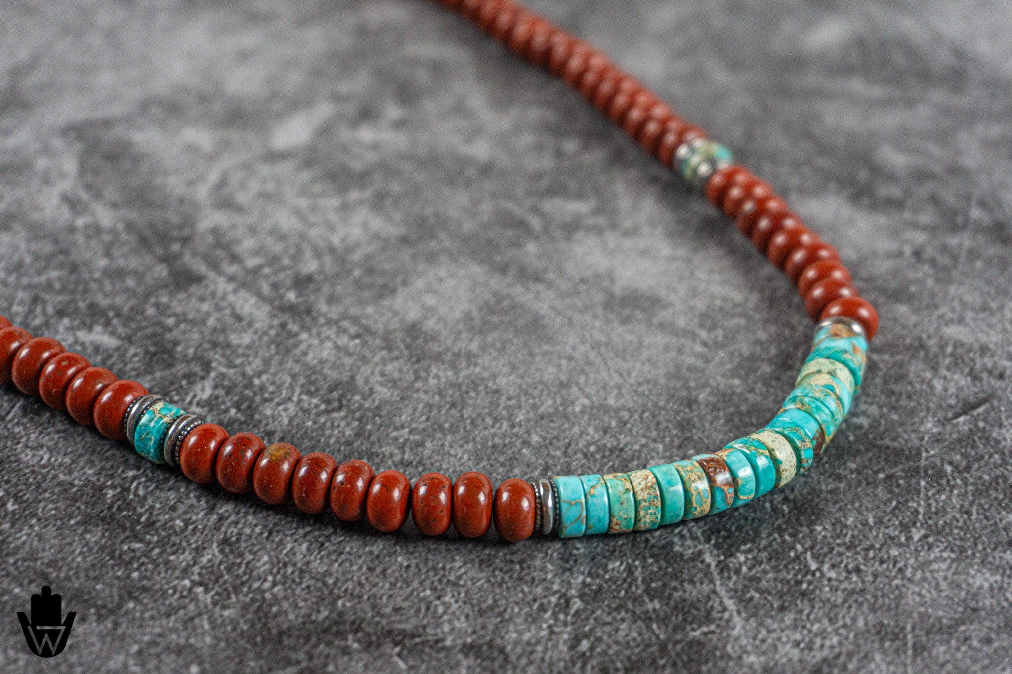 A beaded necklace featuring round reddish-brown beads and a section of turquoise and white striped beads, displayed on a textured gray surface.