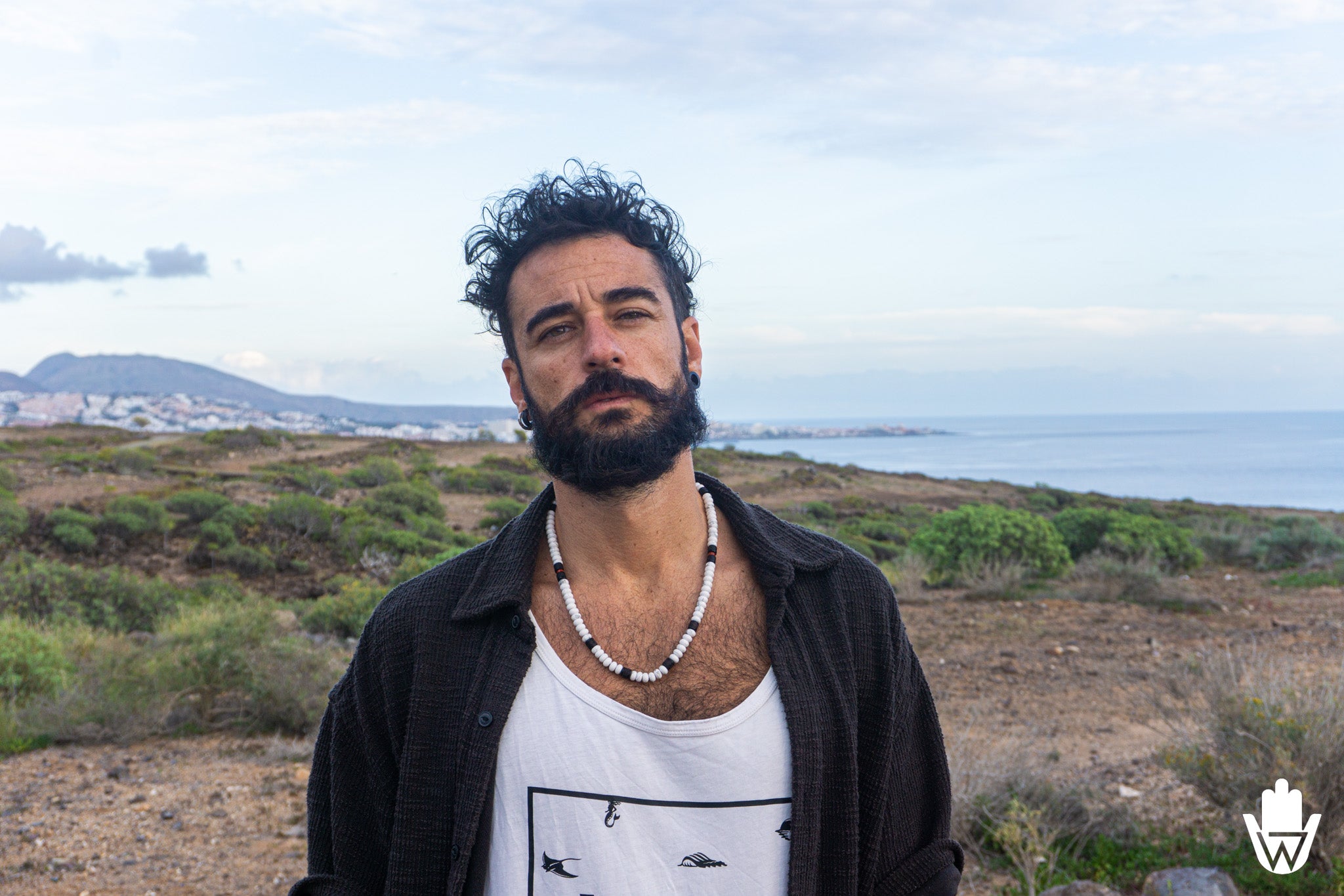 man on a cliff wearing a chunky white necklace