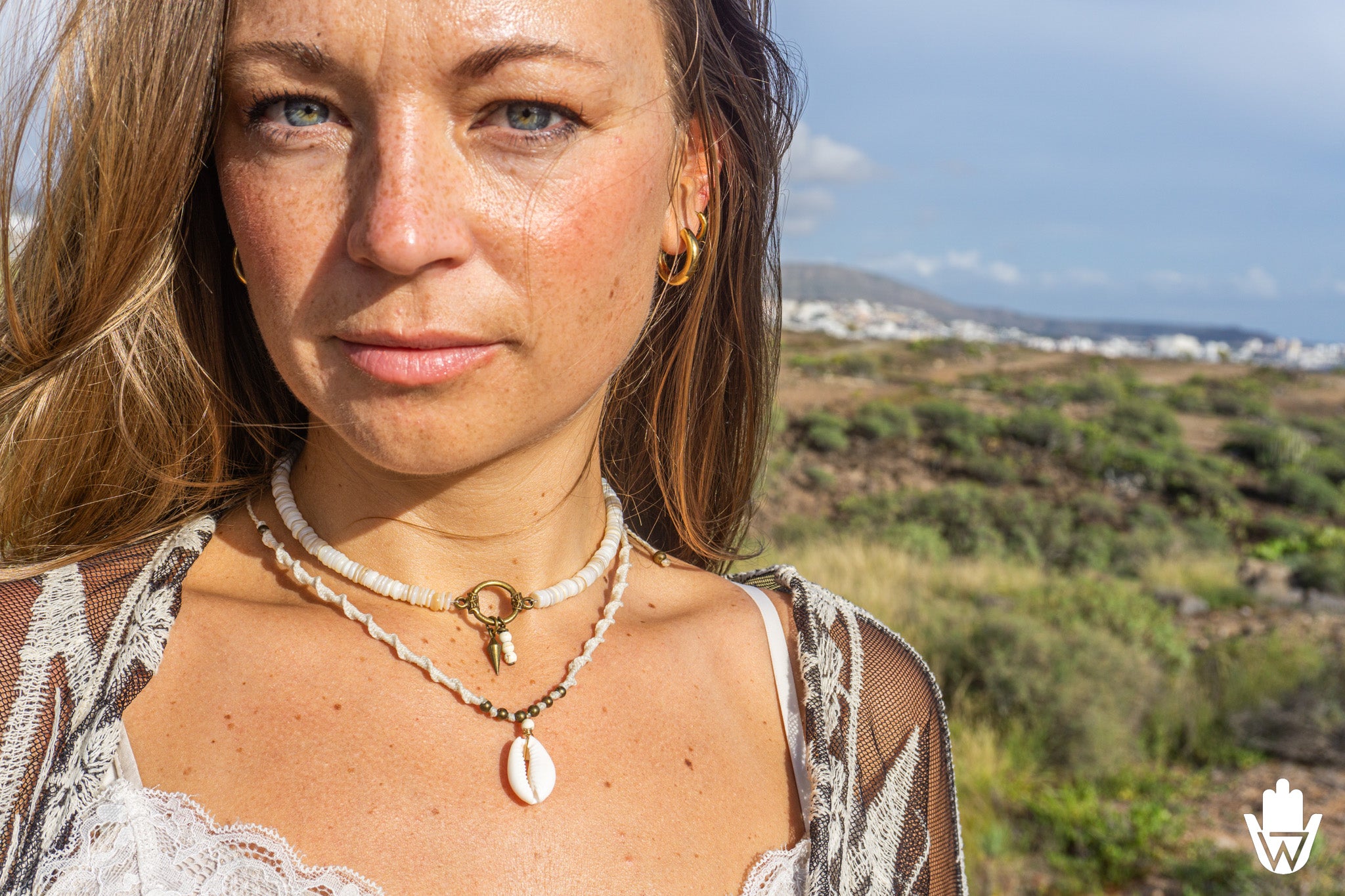 women in a natural landscape wearing a layered necklace set with a cowrie shell as pendant