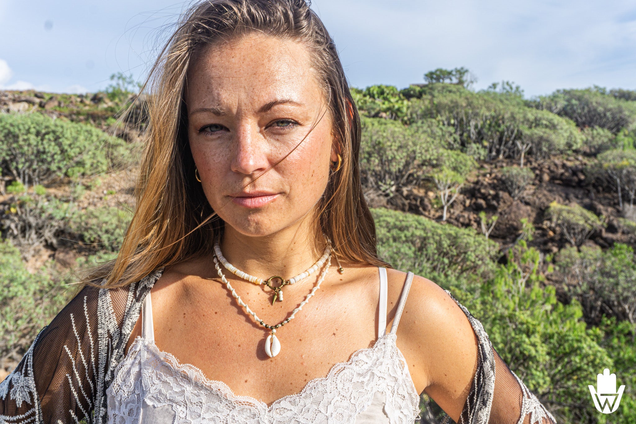 women in a desertic landscape wearinf a white top and a laered choker necklace set with a shell

