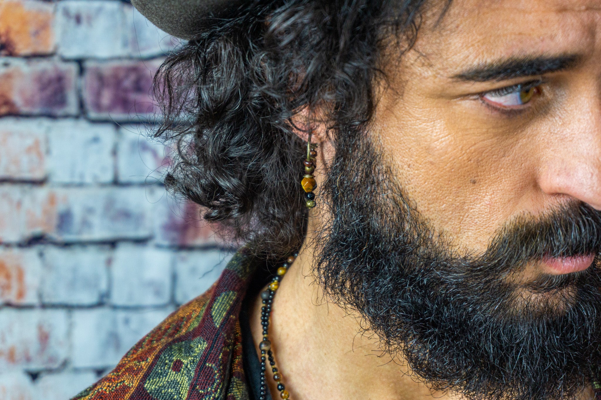 Multi faceted tiger eye stone earring with bronze hoop on a long haired man with a pirate hat and a golden vest
