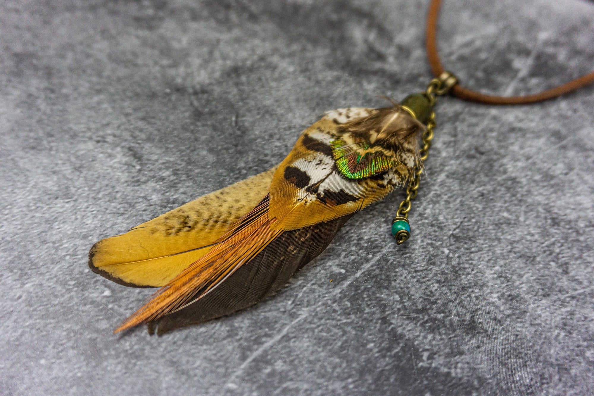 close up to the pendant of the necklace, made of a combination of different feathers