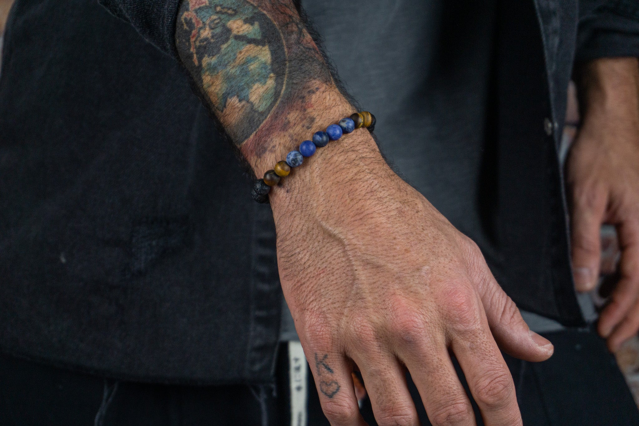 bracelet made of lava stone tiger eye , blue sodalite, weared by a men with a black jacket