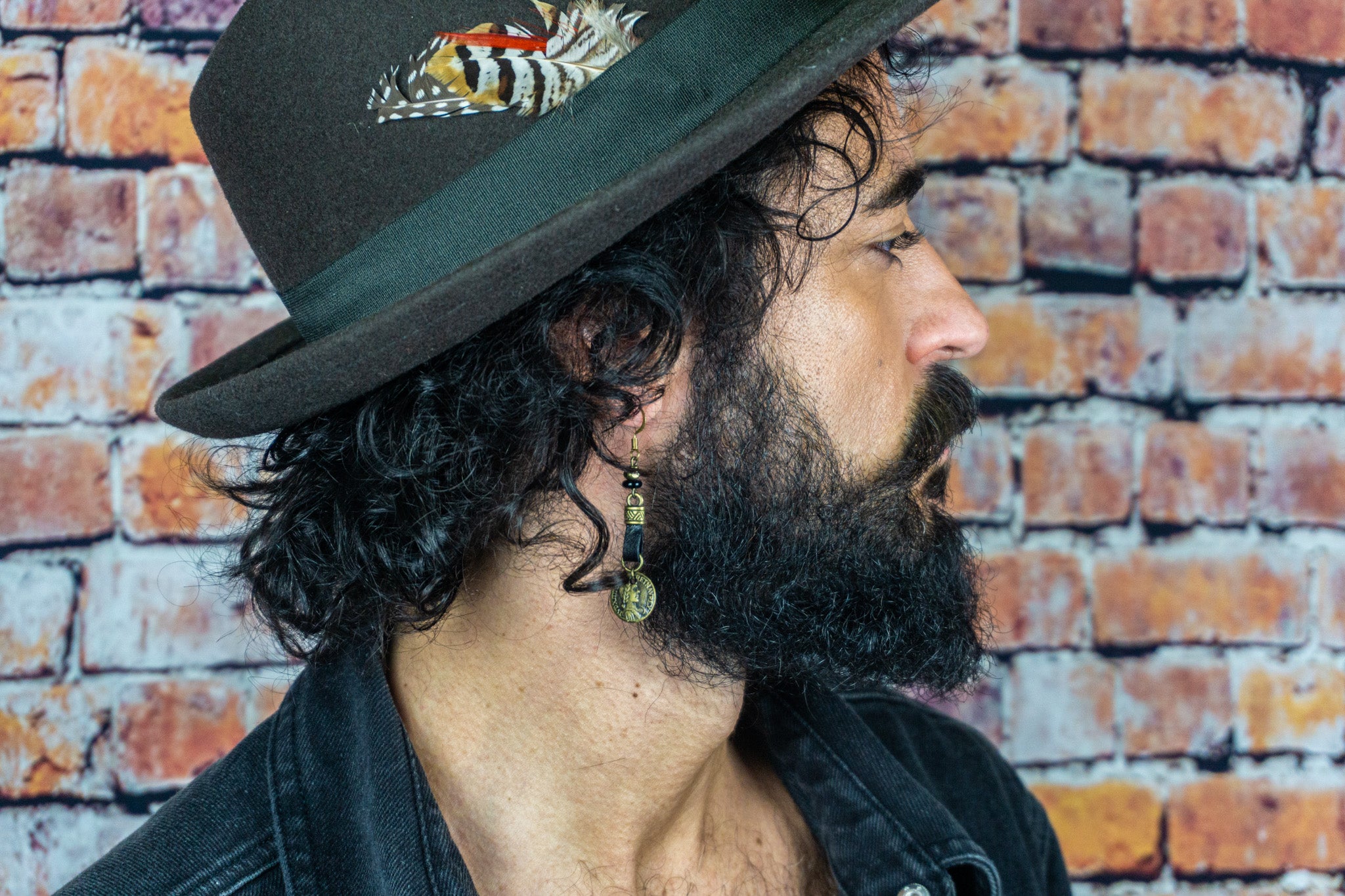 man with curly hair, a hat with a feather and a leather earring with a dangling bronze coin