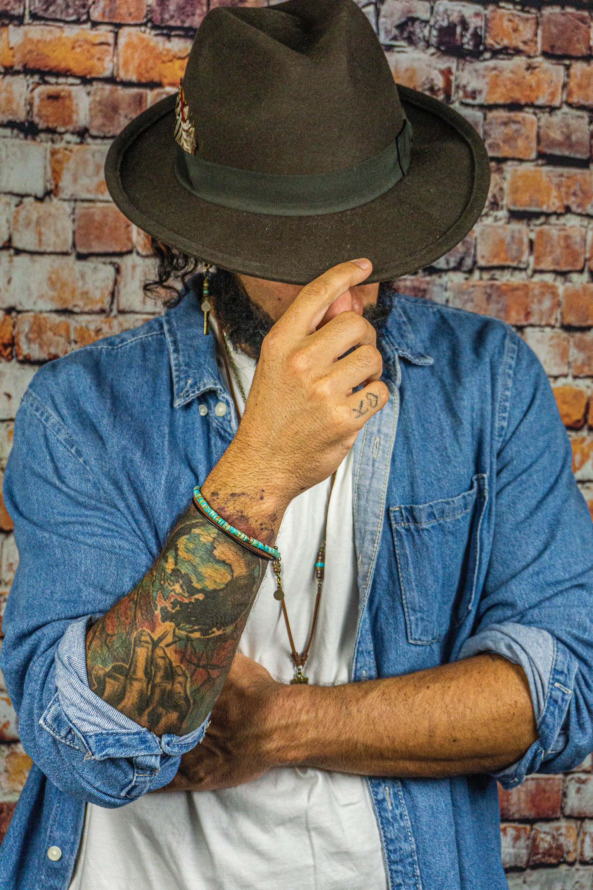 man wearing a hat , showing a layered turquoise and leather bracelet n the wrist