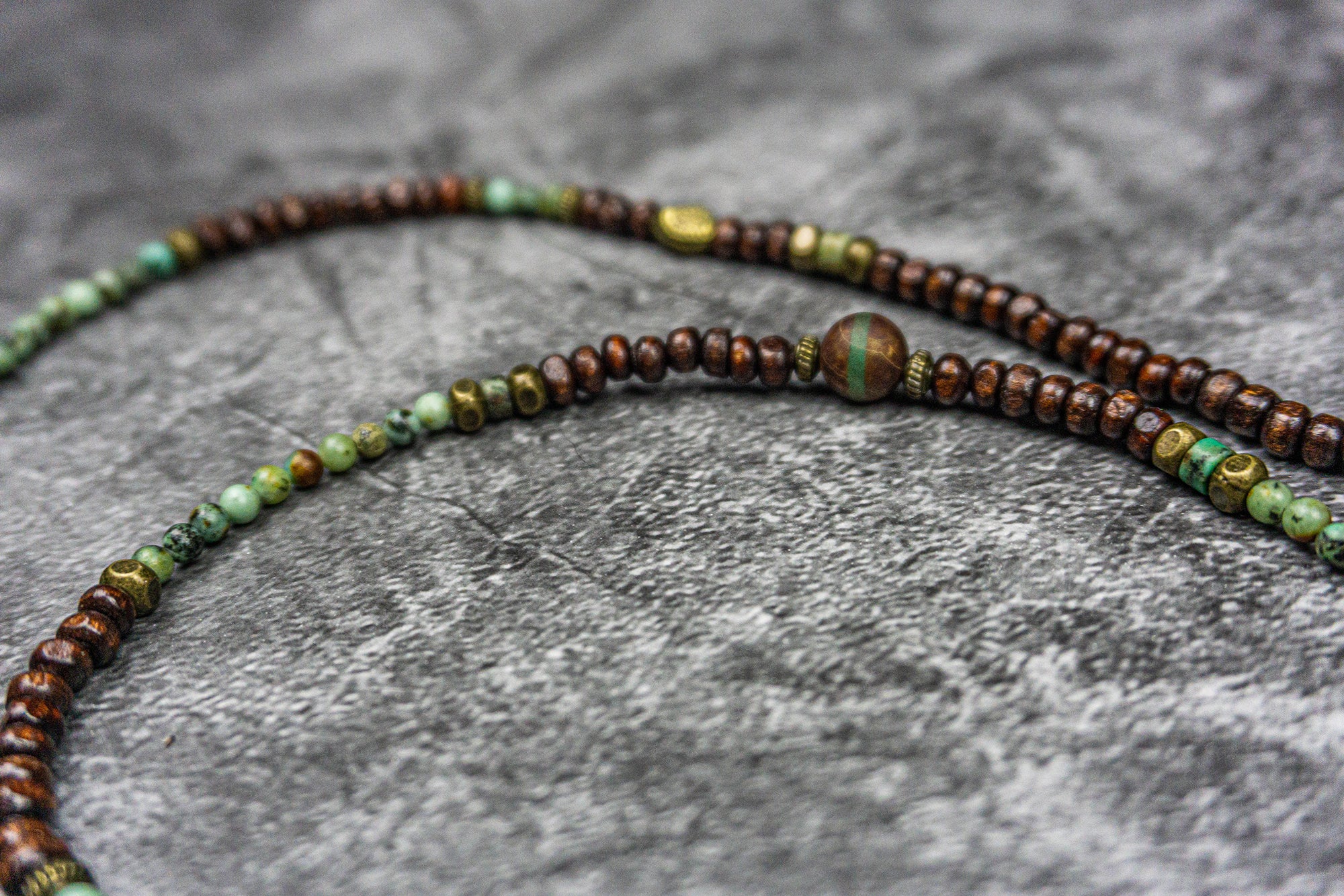 close picture of a  necklace made of wood and green gemstone bads, agate and bronze deatils- wander jewellery