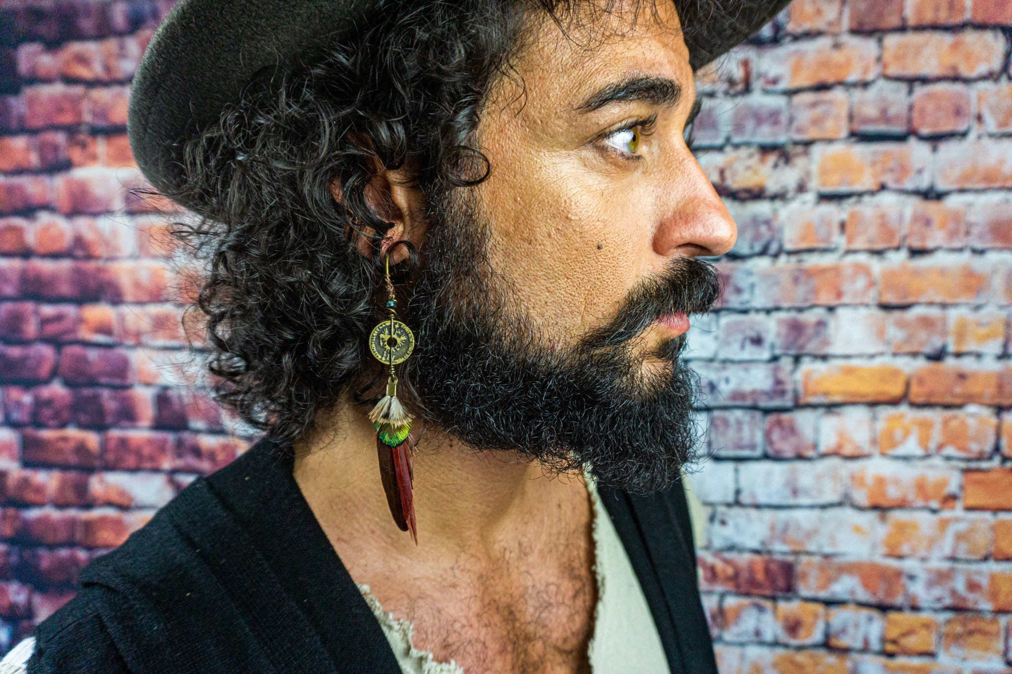 mens with a hat wearing a long red and green feather earring with a coin charm- Wander Jewellery