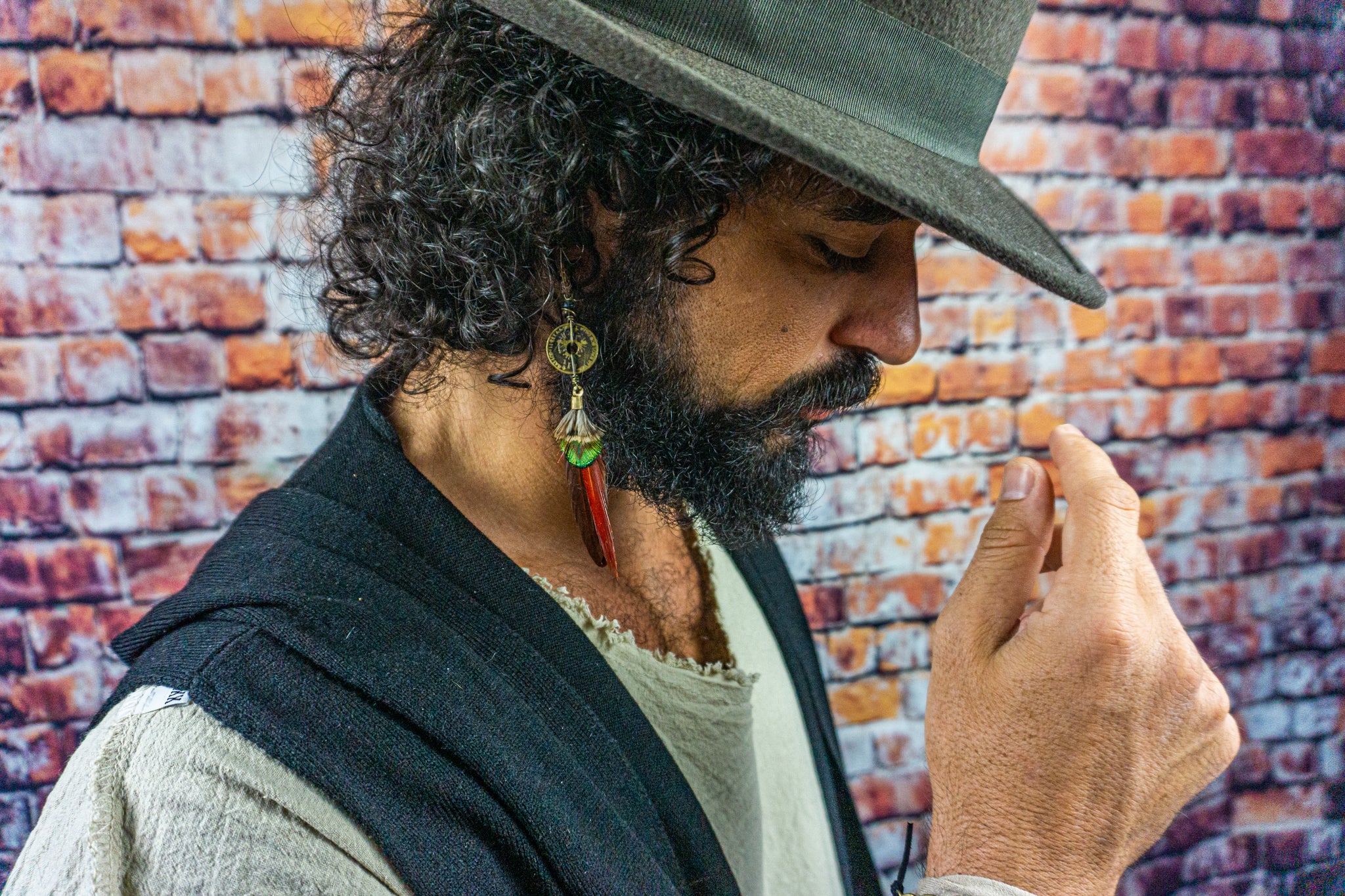 mens with a hat wearing a long red and green feather earring with a coin and gemstone charm- Wander Jewellery